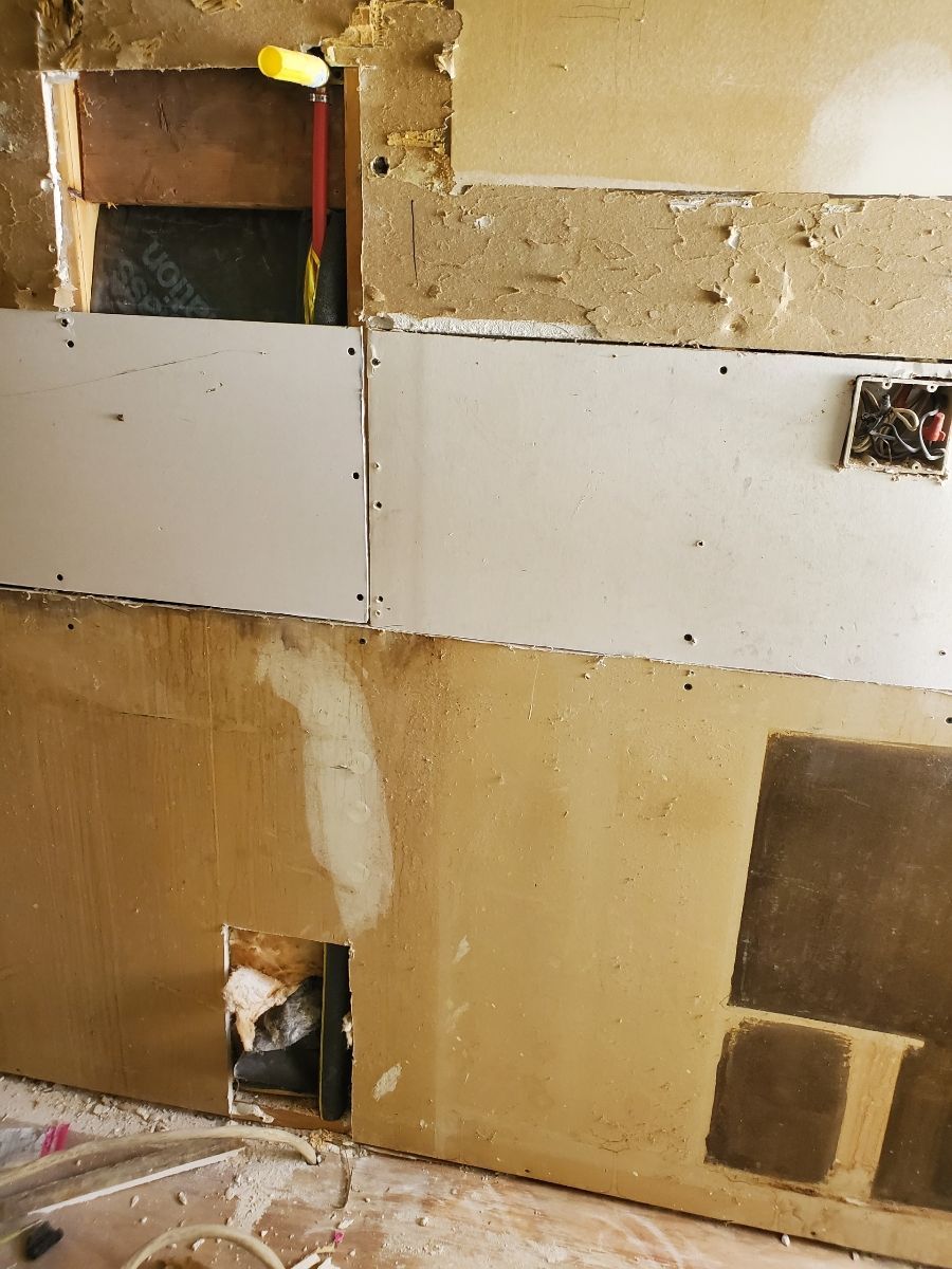 Wall under construction with exposed layers and drywall. Yellow roller rests in a hole.