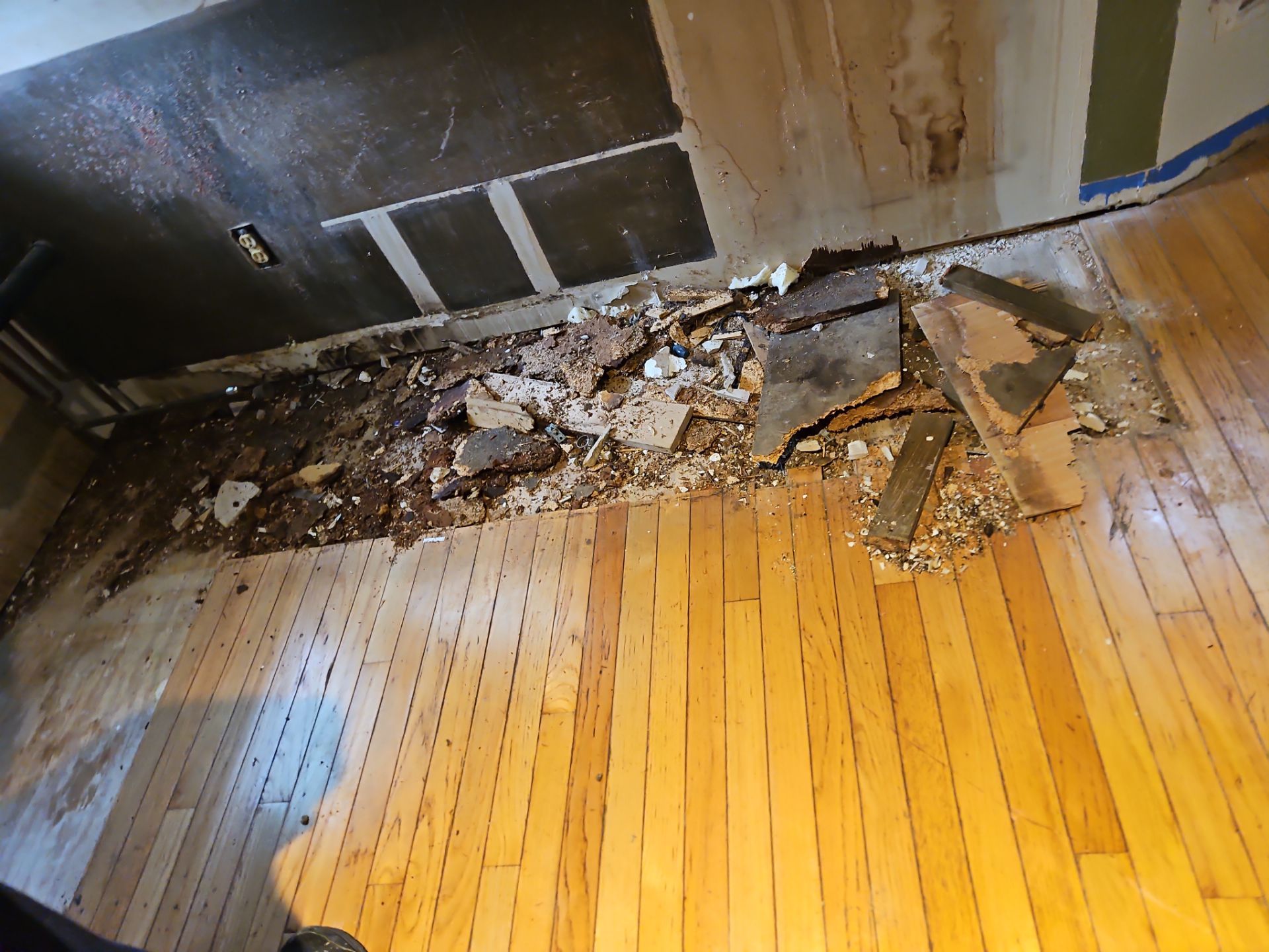 Damaged hardwood floor with debris, likely from ceiling/wall repairs. Room interior, daytime.
