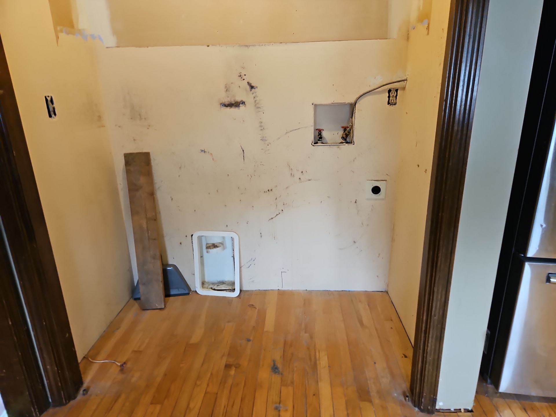 Small, unfinished room with hardwood floors and damaged walls, doorway on either side.