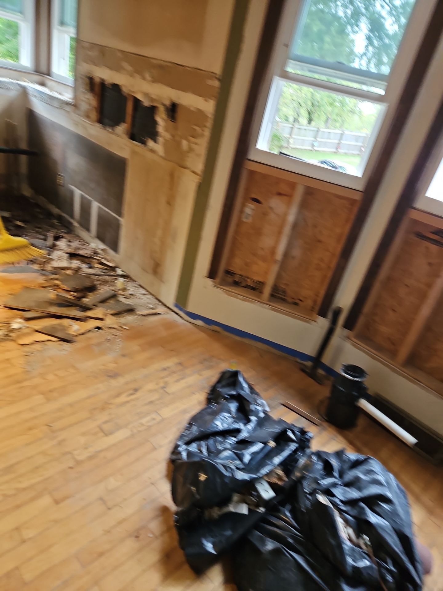 Room under renovation with exposed wall, hardwood floor, windows, and debris.
