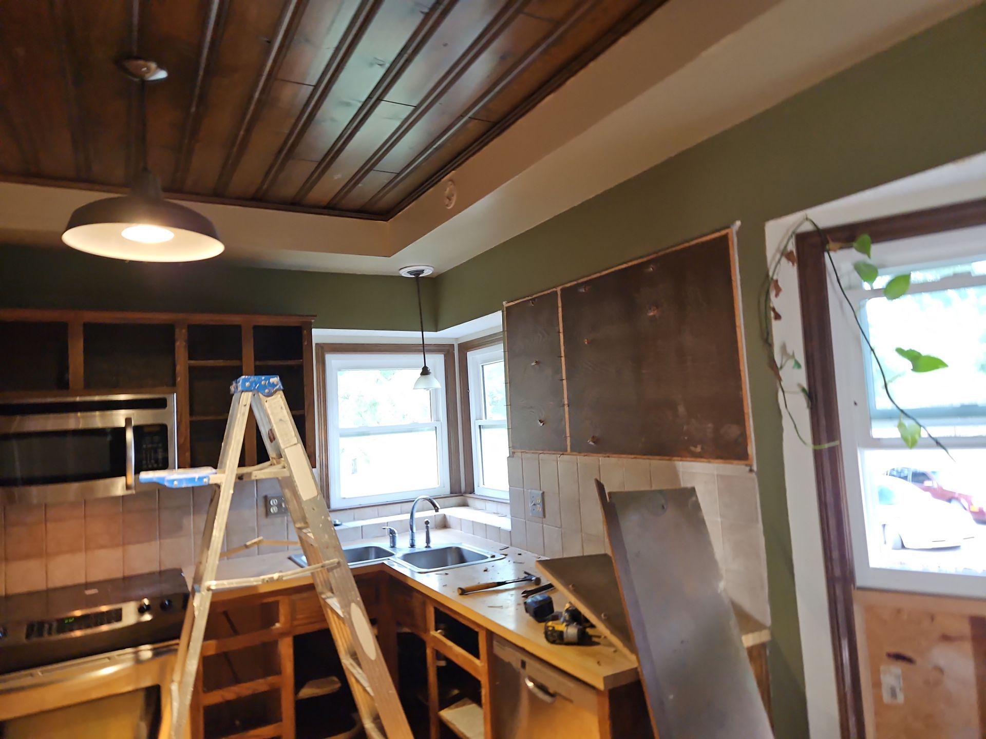 Kitchen under renovation with exposed cabinets and wall, ladder, and wood ceiling.