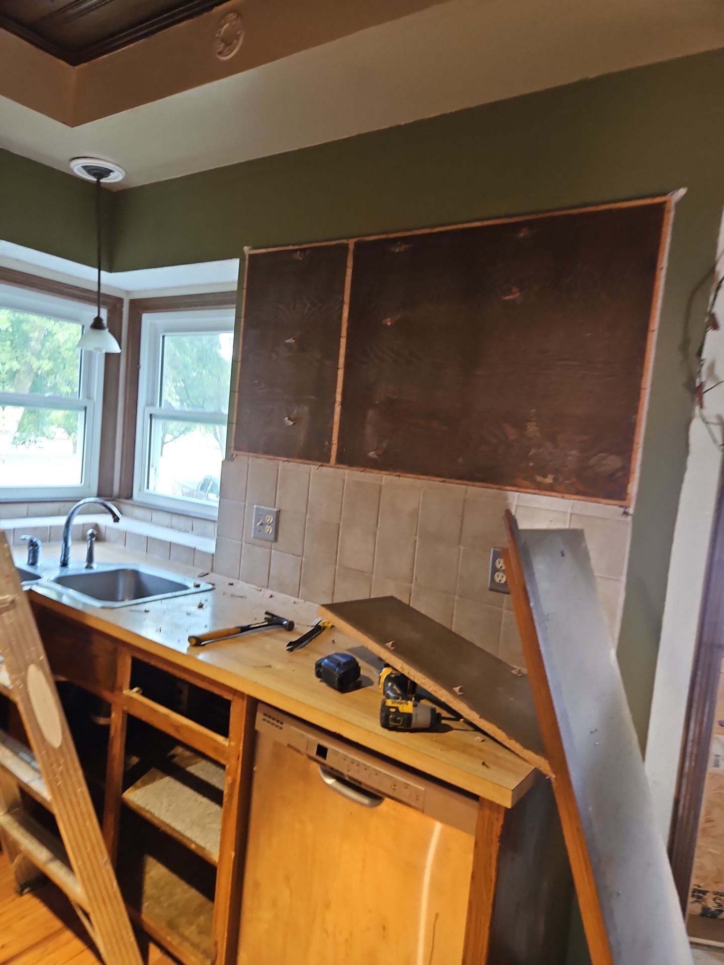 Kitchen renovation in progress: removing cabinets and backsplash, brown walls, windows, and tools visible.