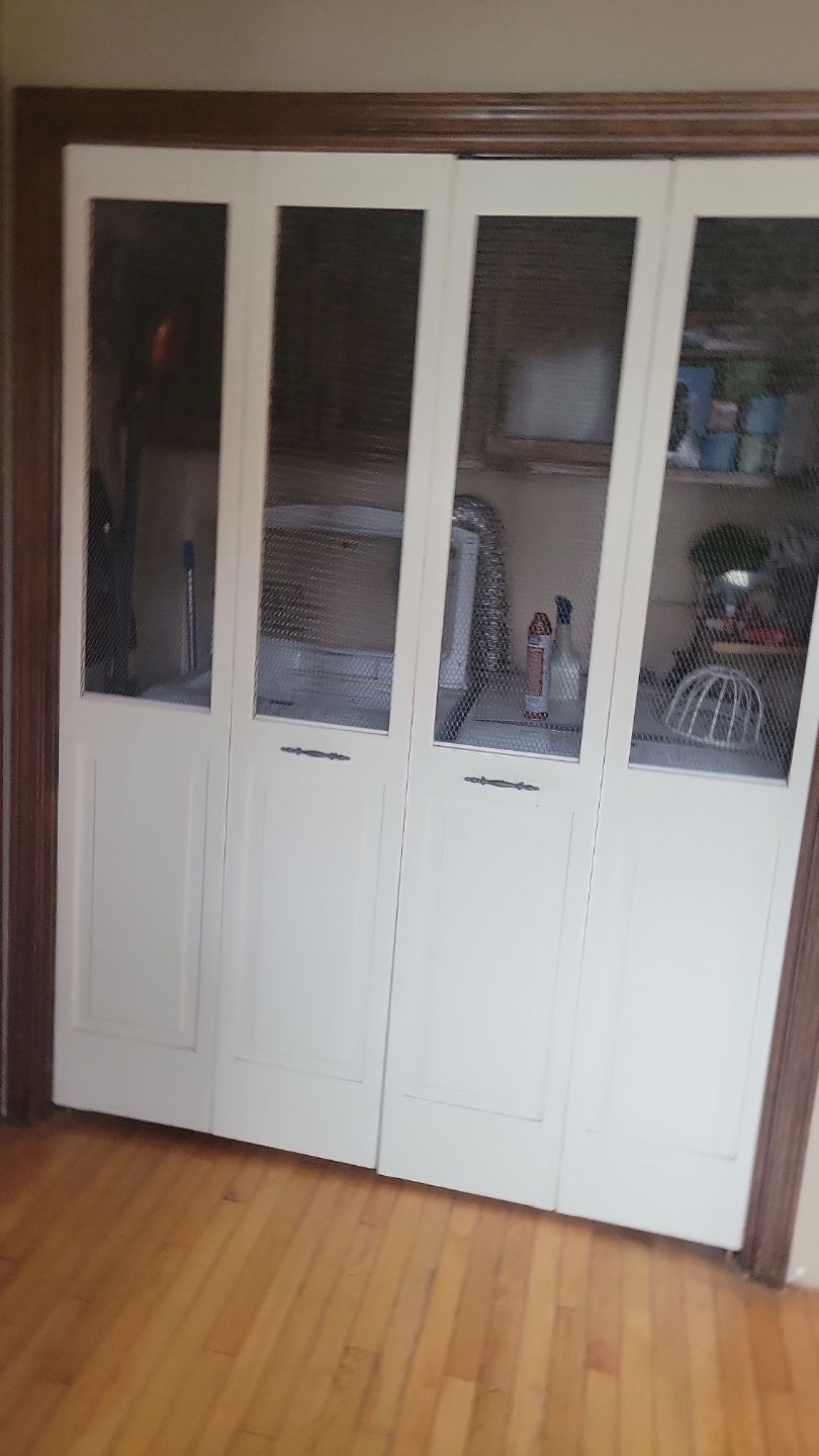 White bi-fold closet doors with glass panels, wooden frame, and hardwood floor.