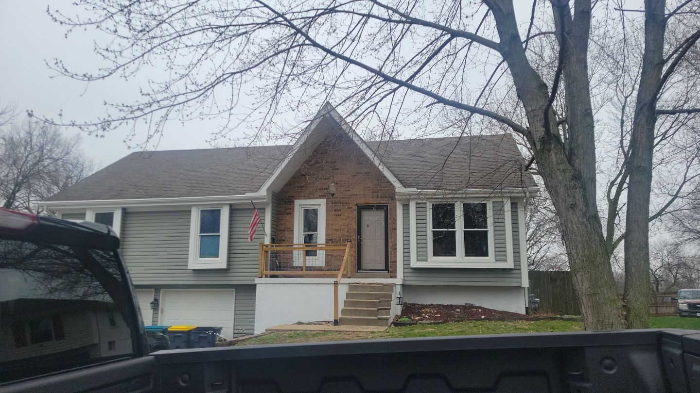 House with brick accent, gray siding, front porch, and bare trees on an overcast day.