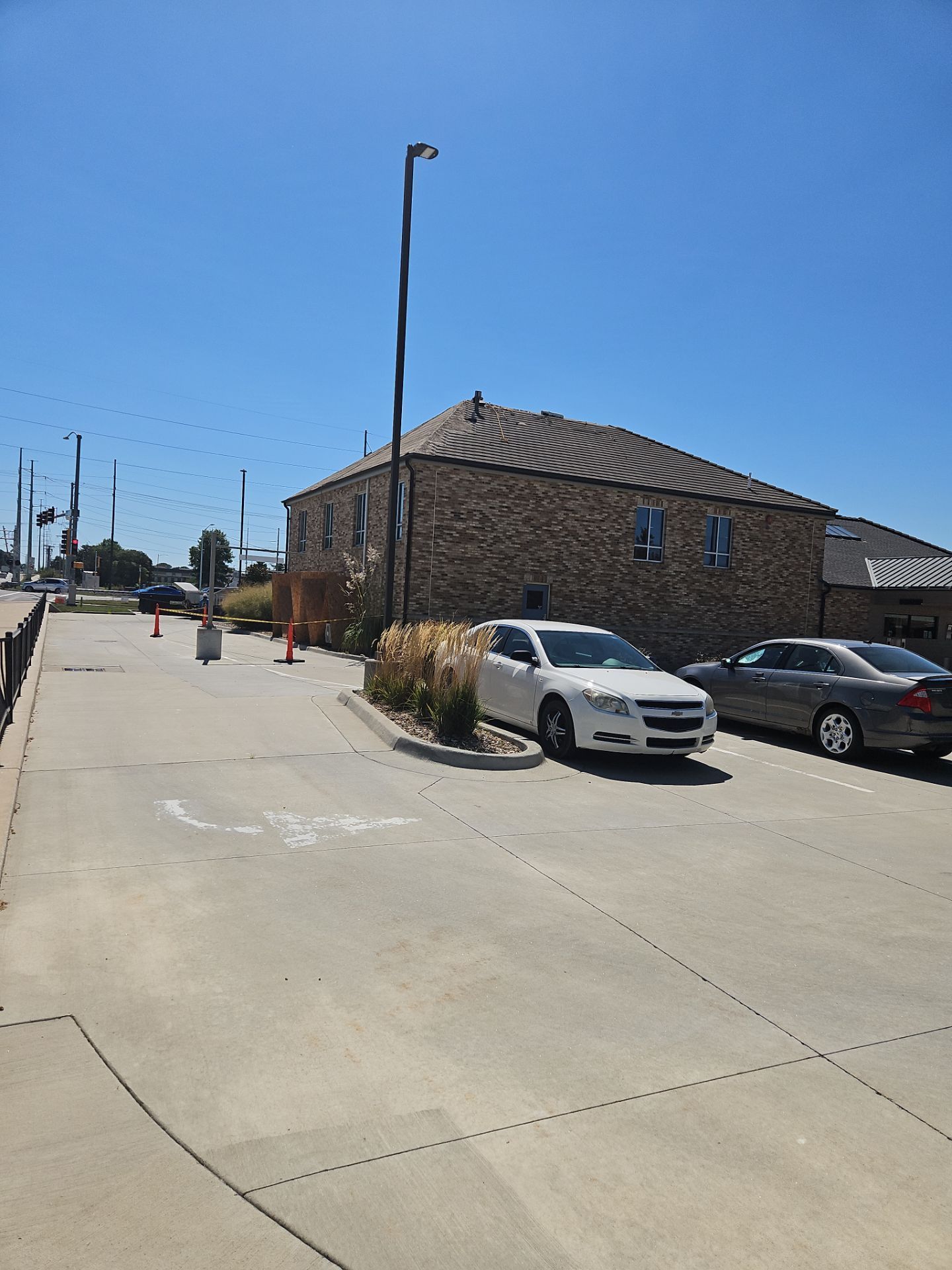 A white car parked near a stone building on a sunny day, with orange traffic cones and a sidewalk.