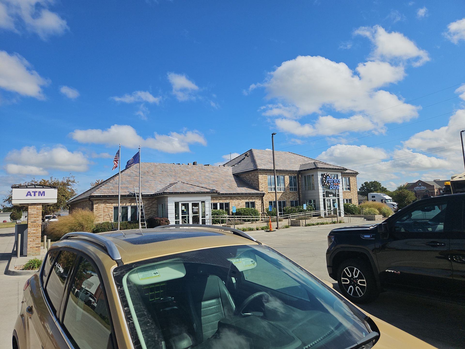 A bank with an ATM, blue sky, and parked cars.