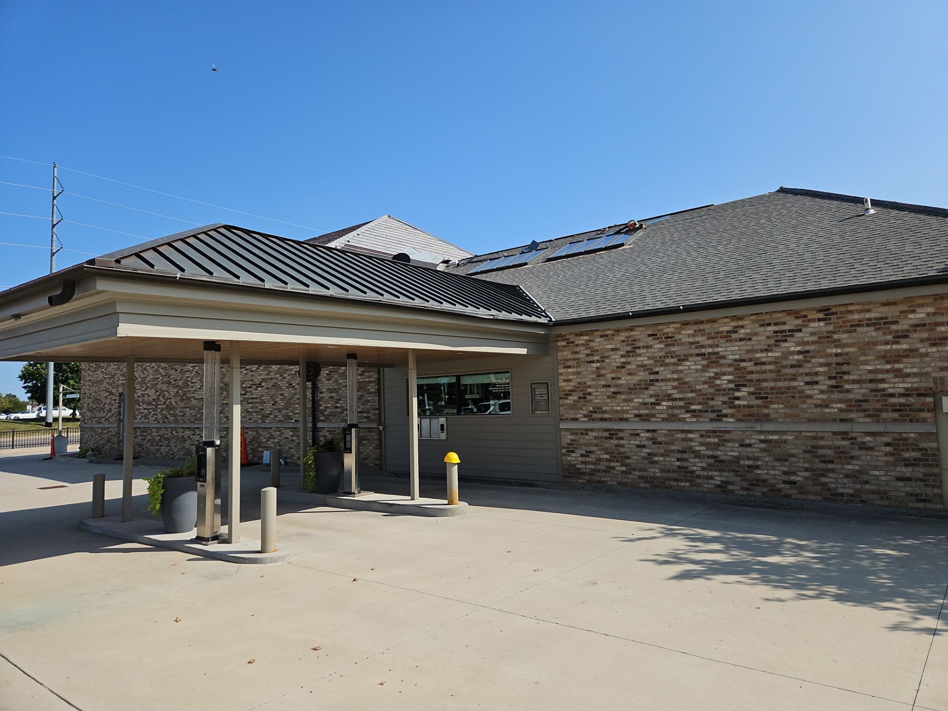 Drive-up bank building with gray roof, beige brick, and clear blue sky.