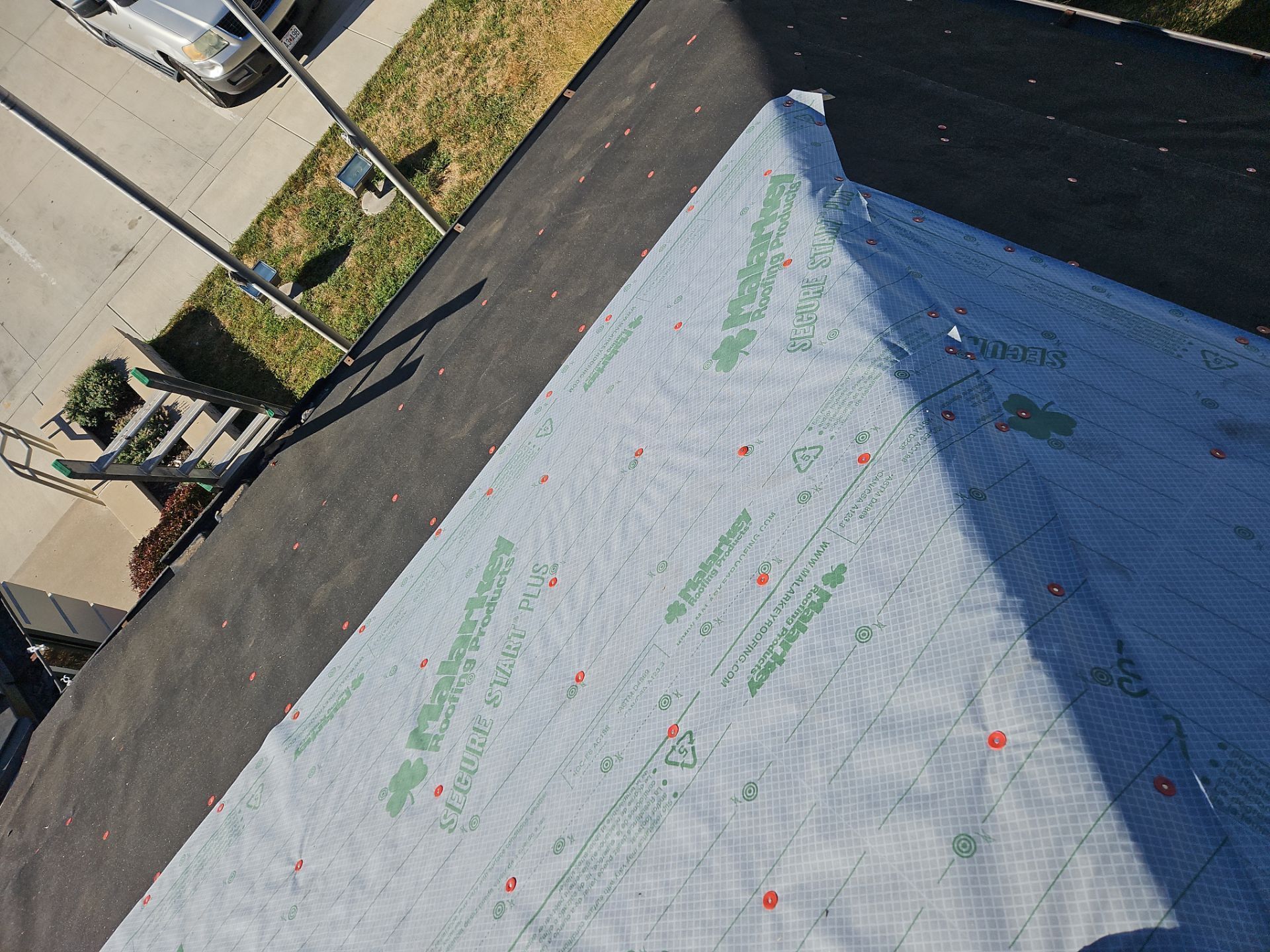 Rooftop, with underlayment, ready for shingles. View includes asphalt shingles and some ground with cars.