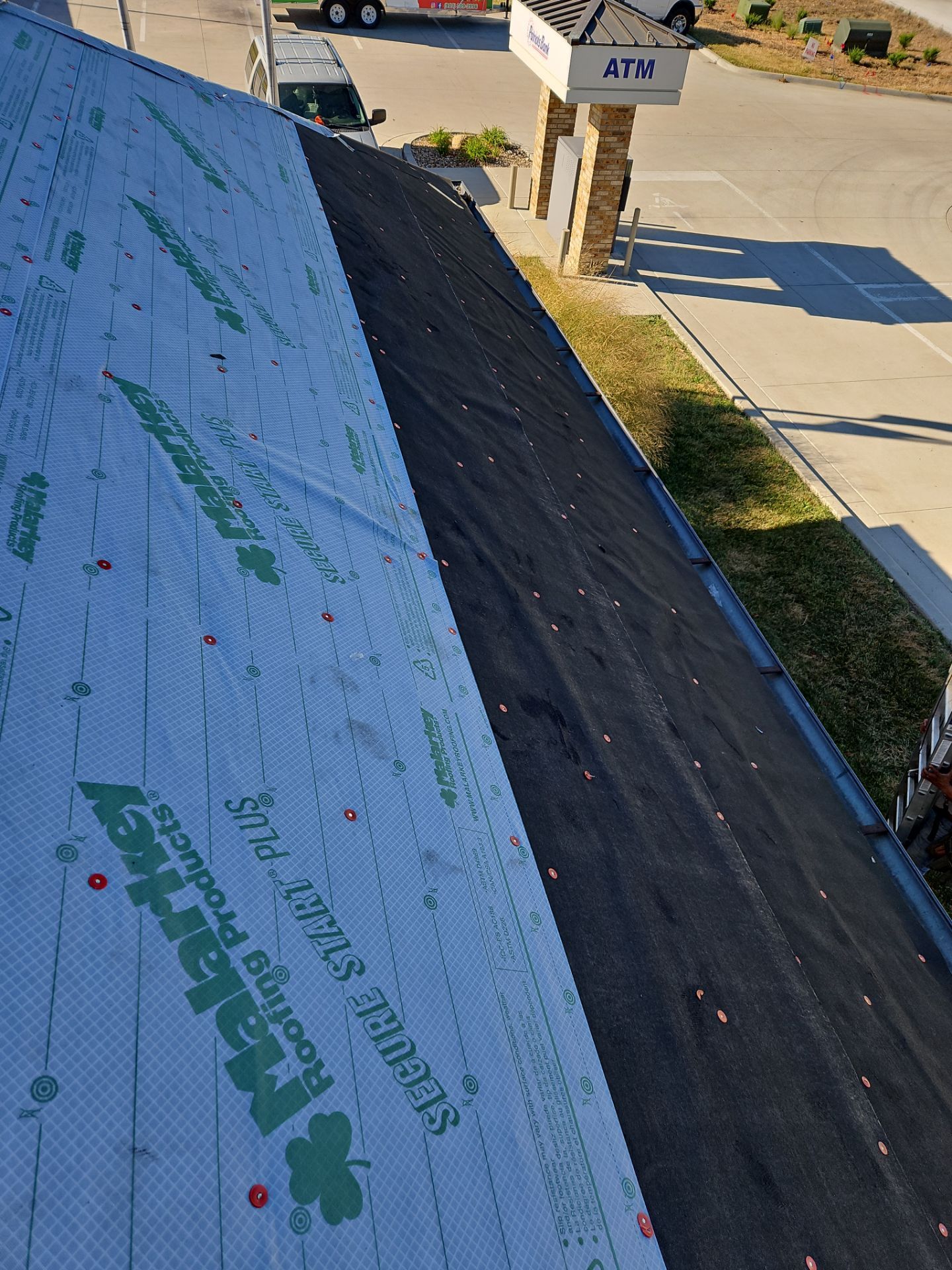 Roofing work in progress: one side with underlayment, other with old shingles. Sunlight.