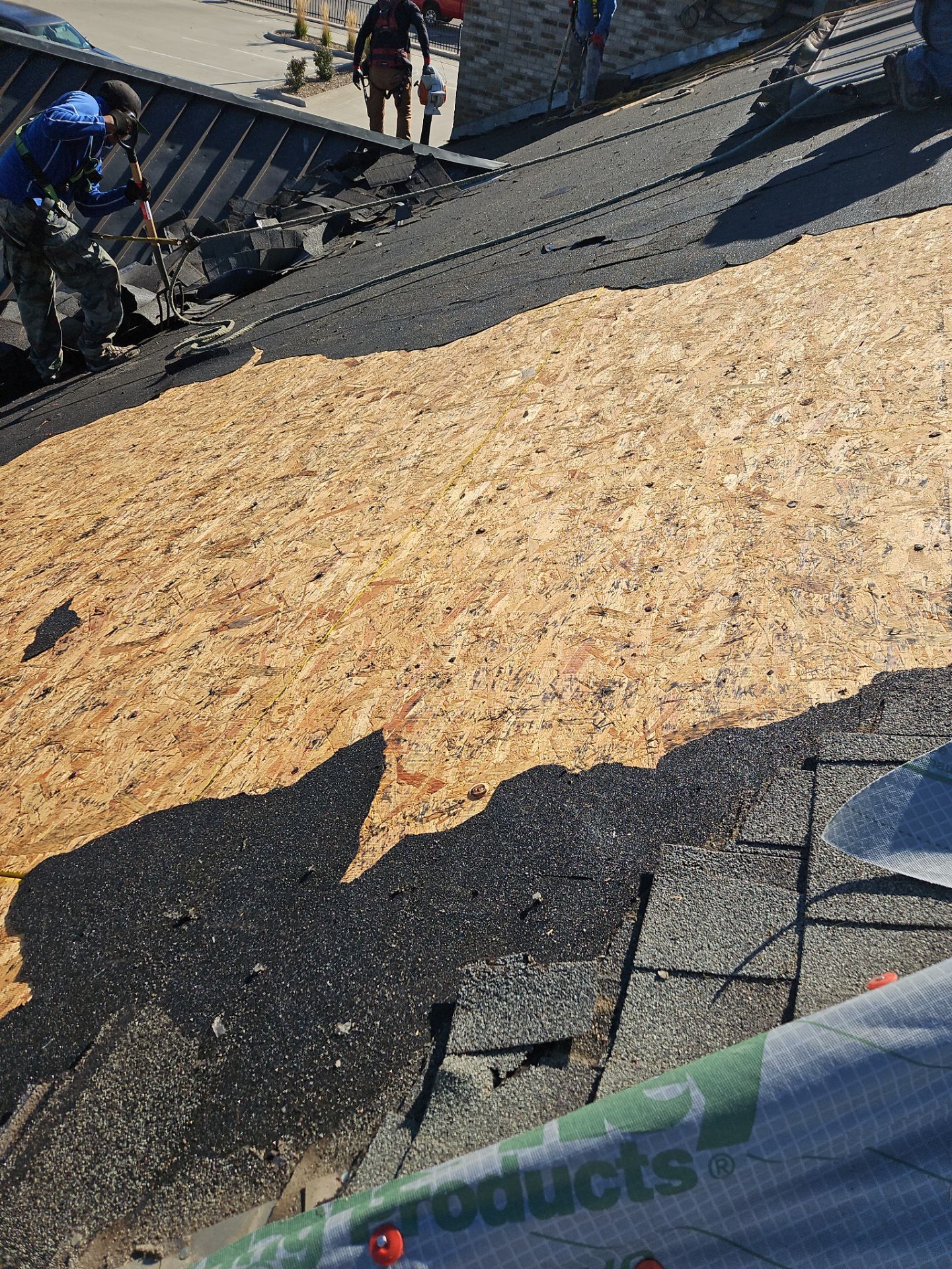 Construction workers replacing roofing material on a building. One man is removing old shingles while others work further up.