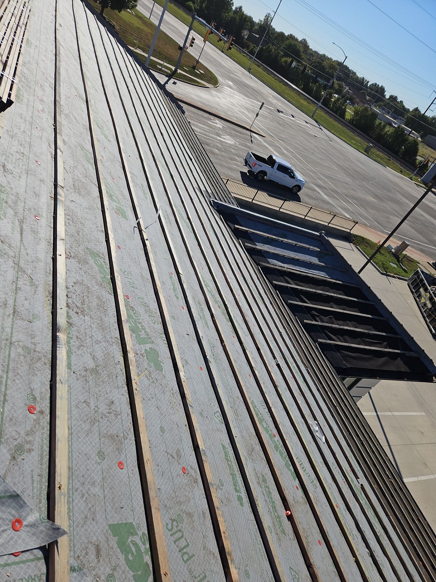 Rooftop with long wooden planks, overlooking a road with a white pickup truck parked nearby on a sunny day.