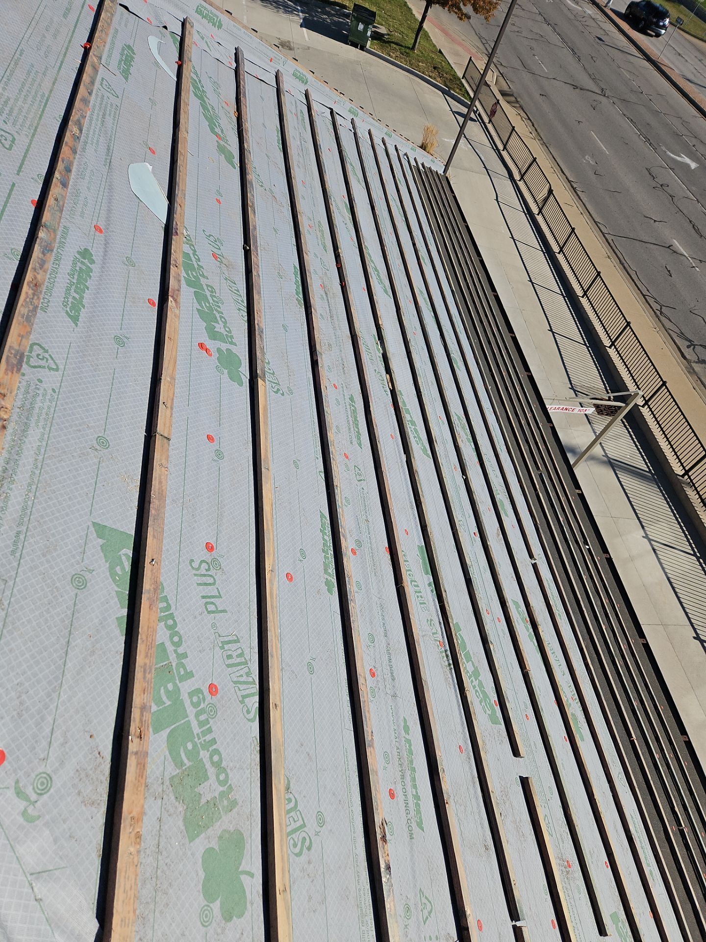 Rooftop under construction with wooden beams, gray membrane, and a road in the background.