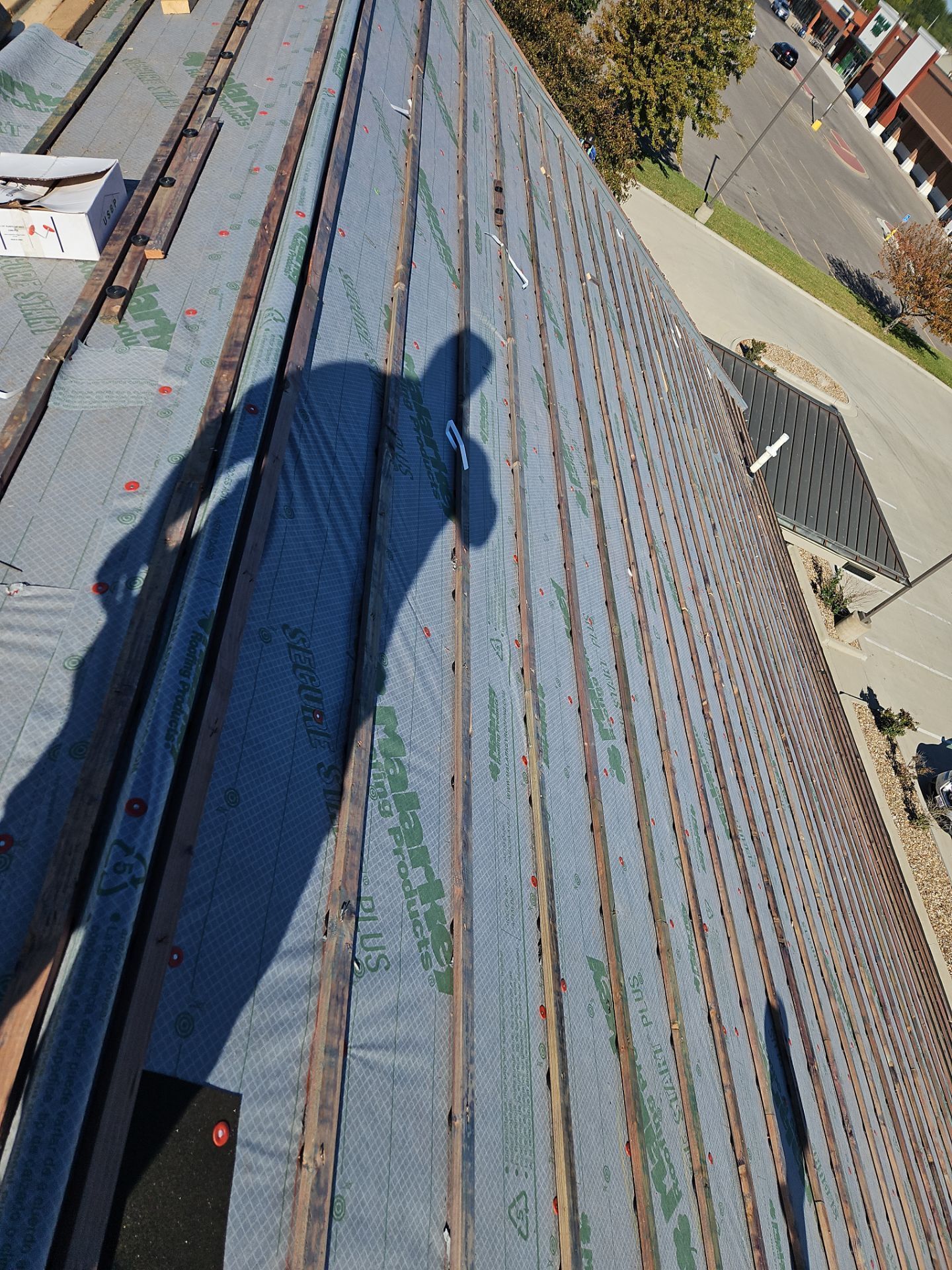 Shadow of person on rooftop with boards and black underlayment.