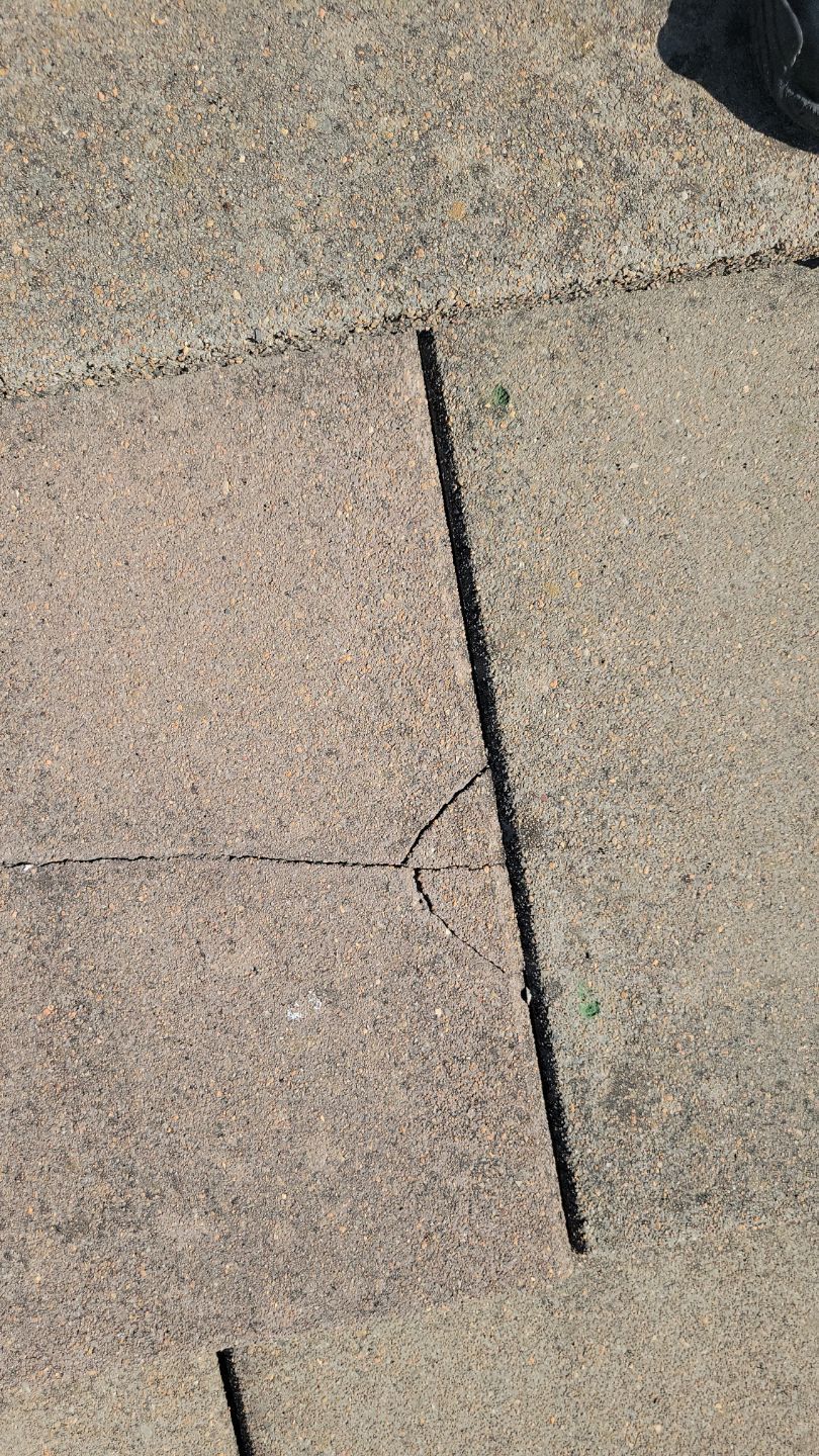 Cracked concrete sidewalk with a long, straight crack and smaller intersecting crack.