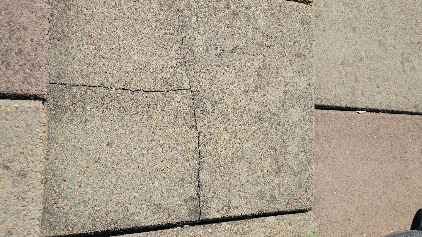 Close-up of a cracked, light-colored concrete paver on a patio.