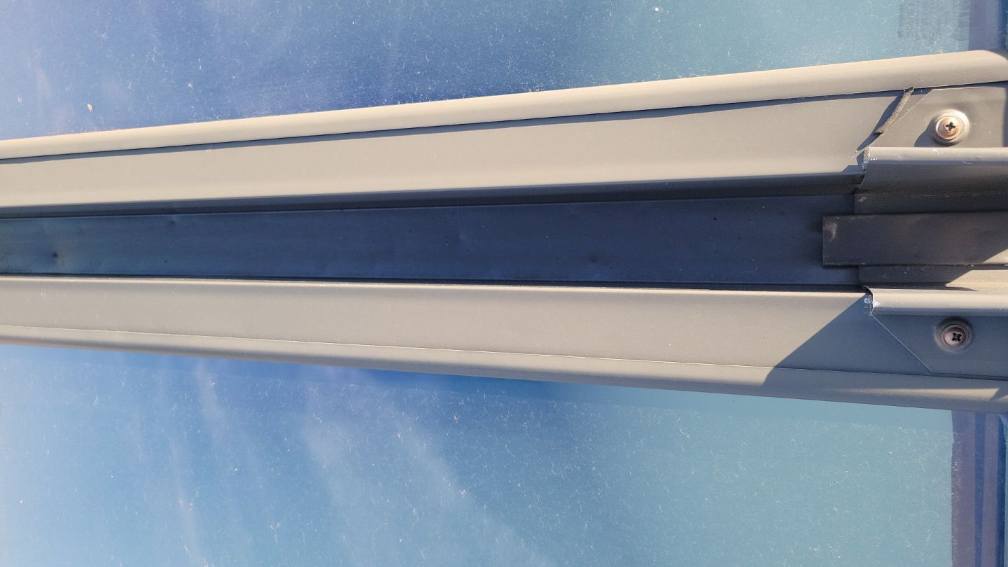 Gray metal frame section with visible screws, against a blurred blue sky background.
