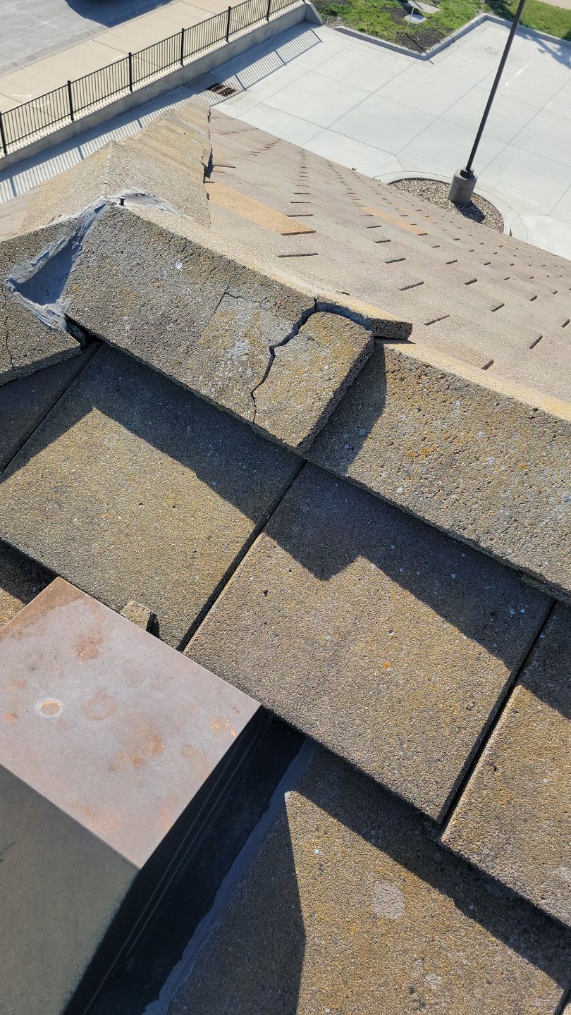 Cracked asphalt roof shingles on an angled roof. Sunlight and shadows are visible.