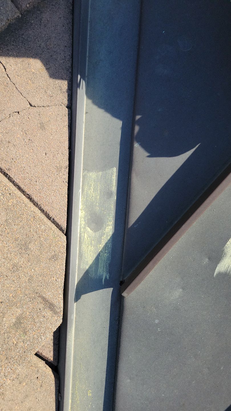 Dark metal flashing next to brown asphalt shingles, angled perspective with shadow.