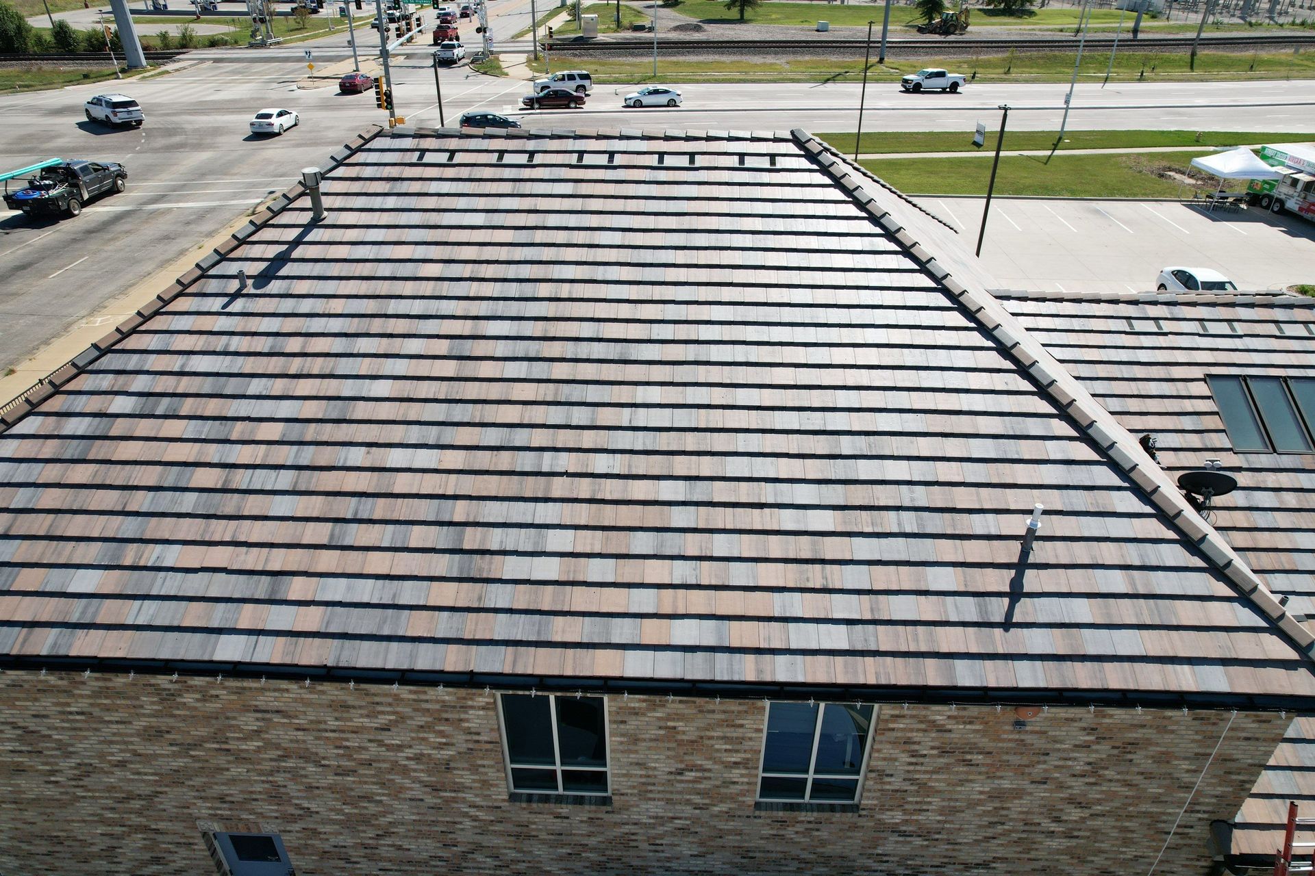 Rooftop with multi-colored shingles. Two windows below. Street and cars visible in the background.