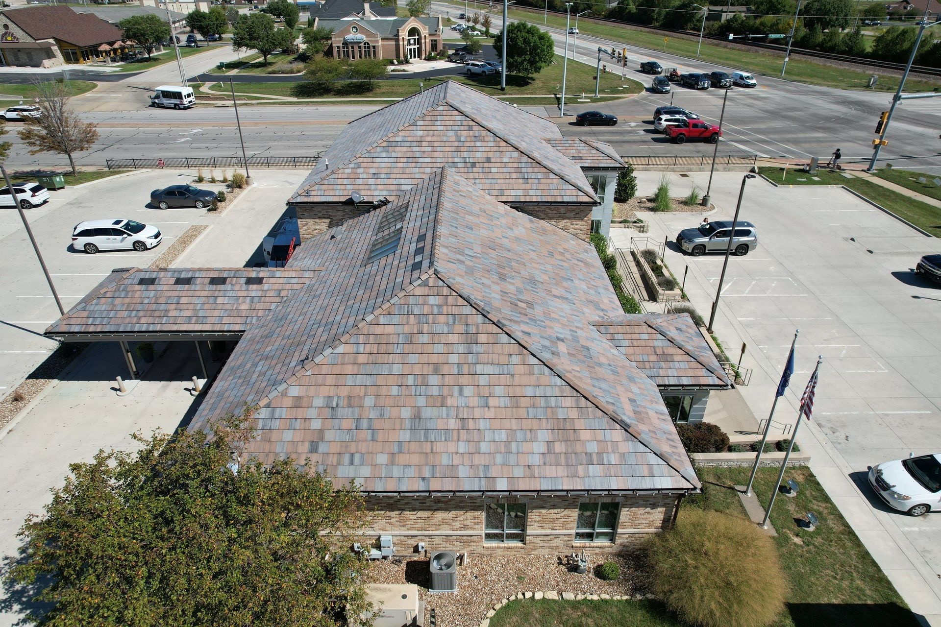 An aerial view of a brick building with a multi-tone tiled roof, surrounded by parking and a street.