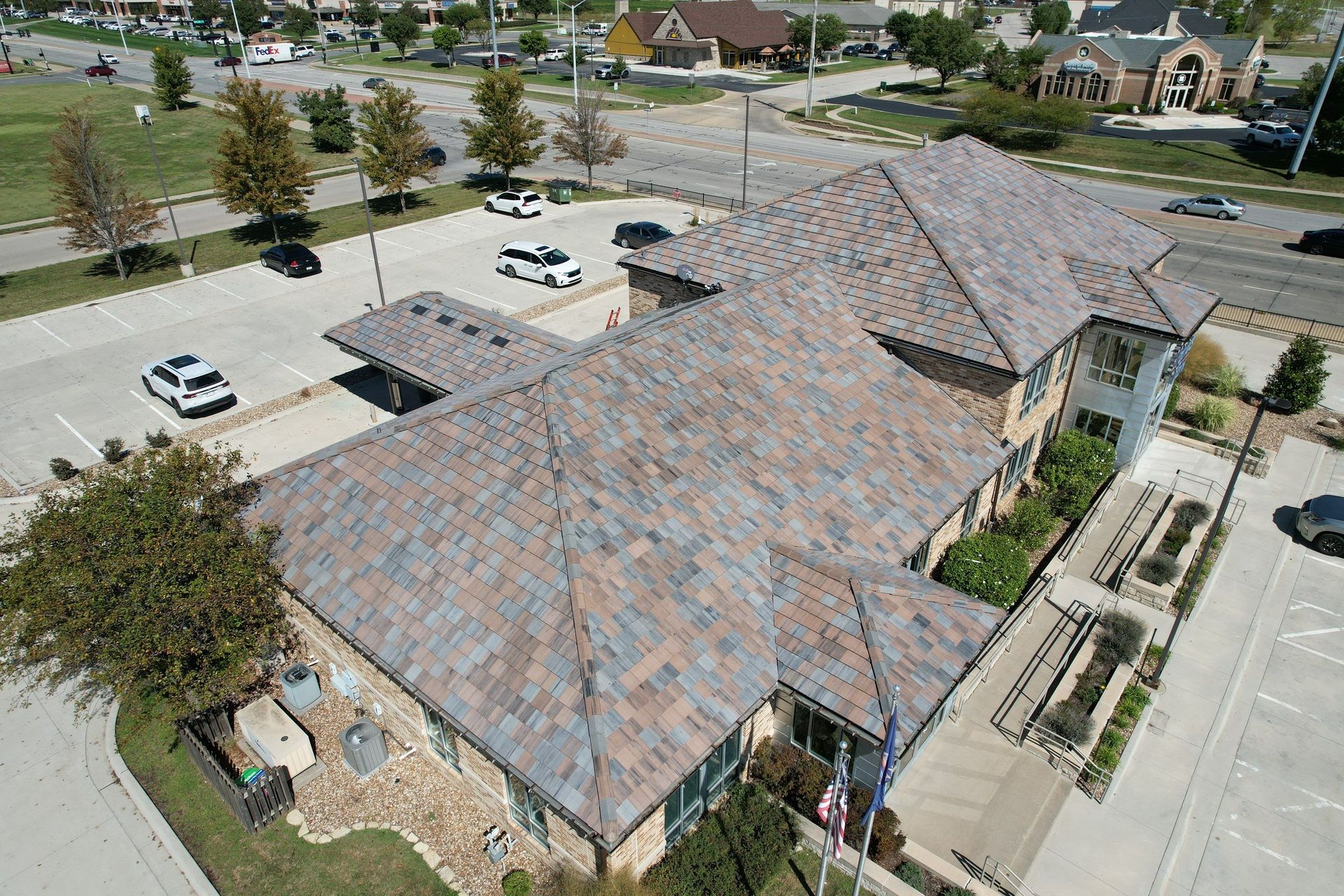 An aerial view of a building with a multi-toned roof, surrounded by a parking lot and green spaces.