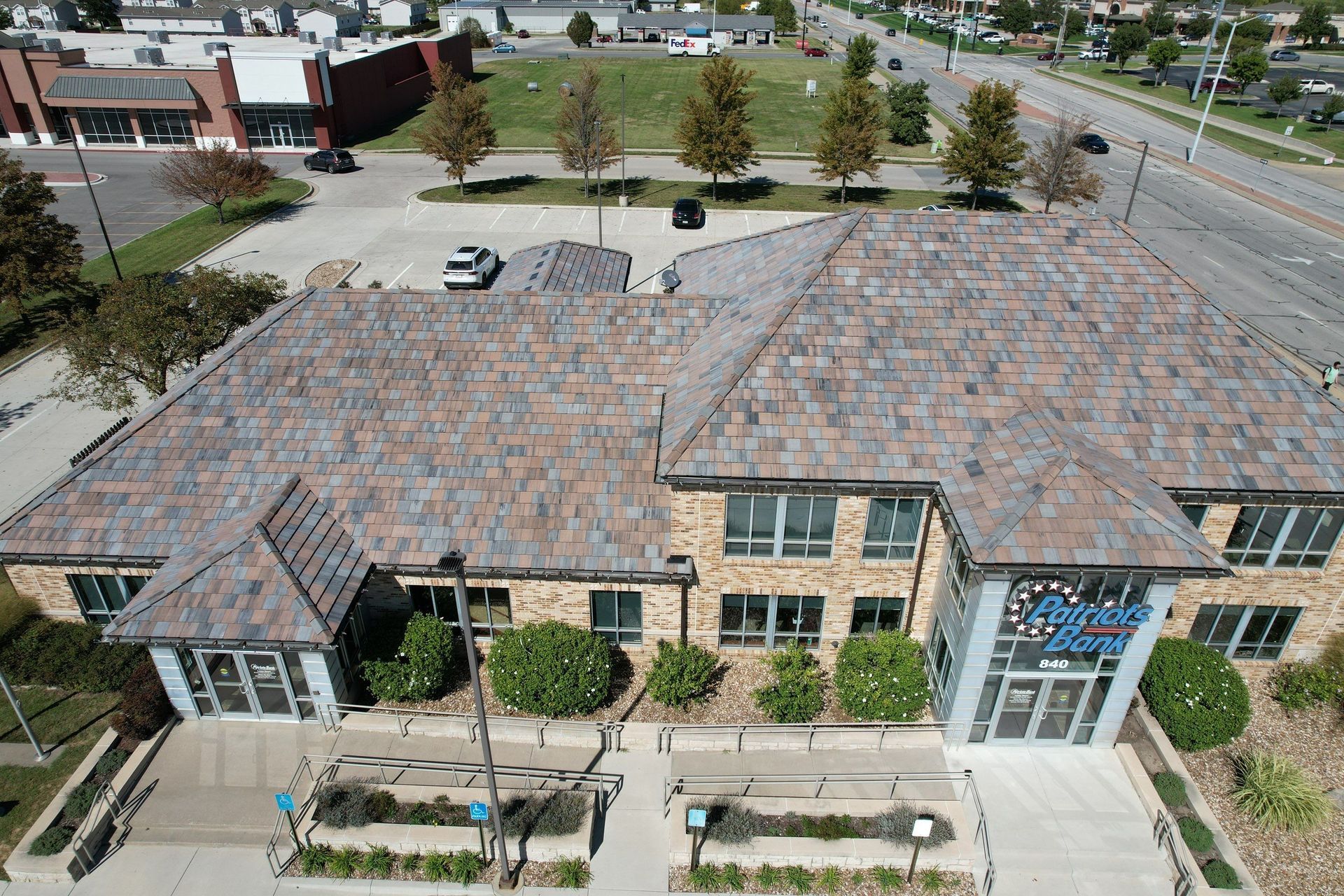 Building with a stone-look roof and brick facade, trees, and sidewalk in front, viewed from above.