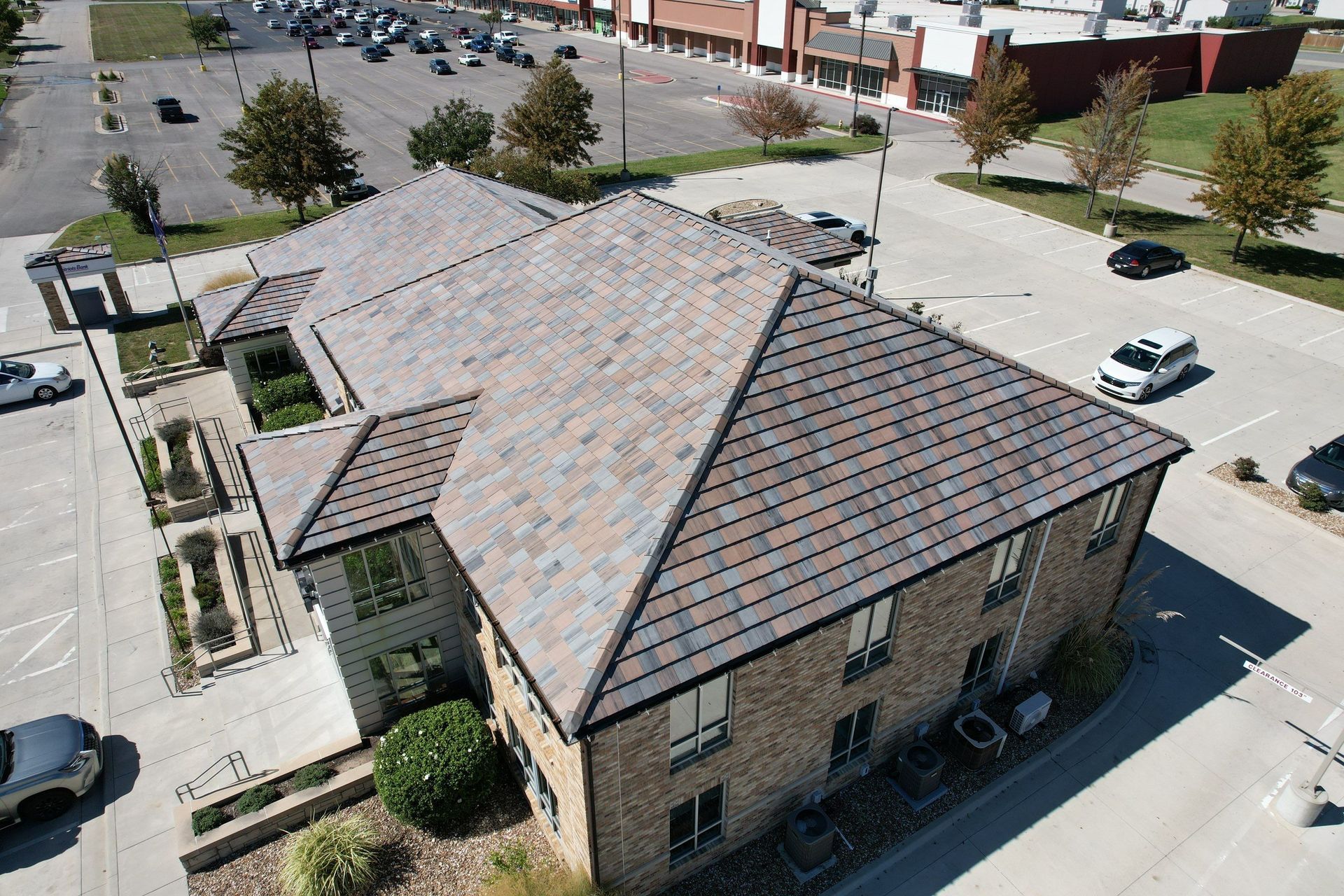 Aerial view of a building with a slate roof, surrounded by parking, trees and other buildings.
