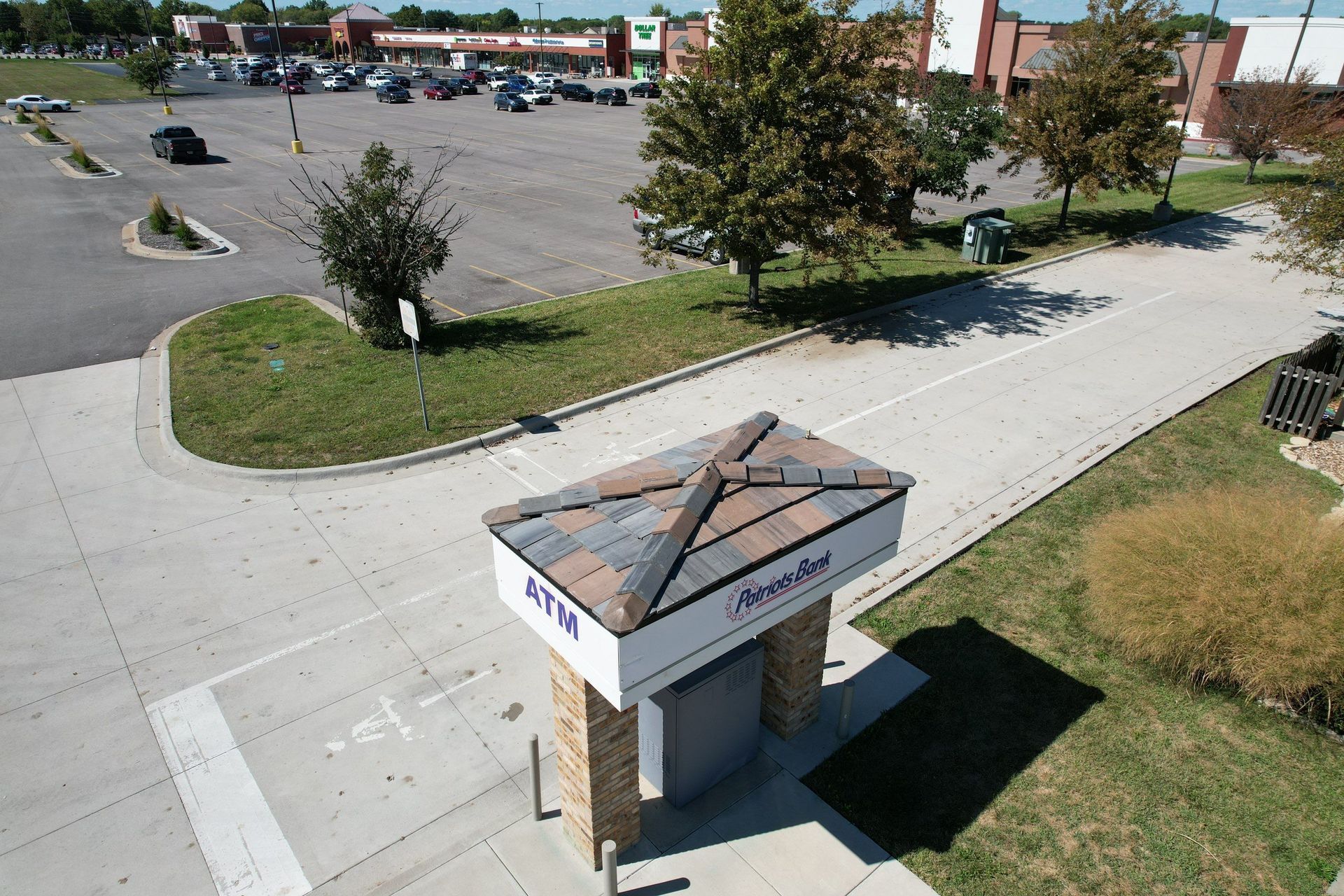 ATM kiosk with patterned roof, in a parking lot, with cars and businesses in the background.