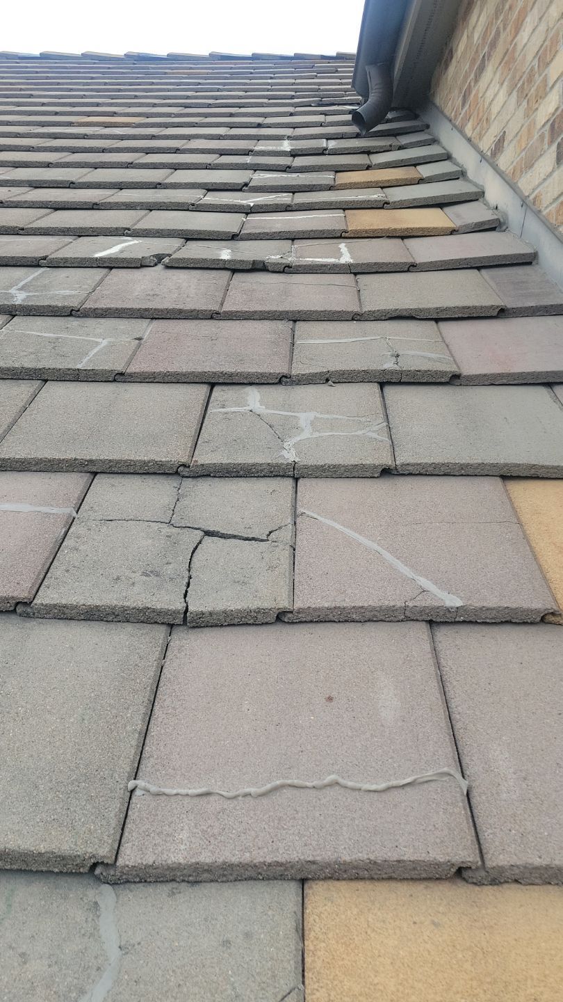 Close-up of cracked gray roof tiles with white chalk markings, near a brick wall and gutter.