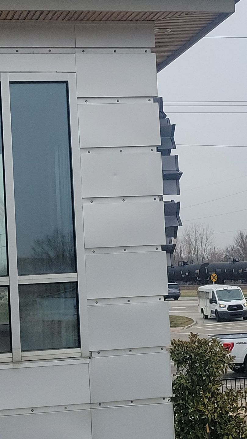 Exterior building corner with warped, light gray siding next to a window.