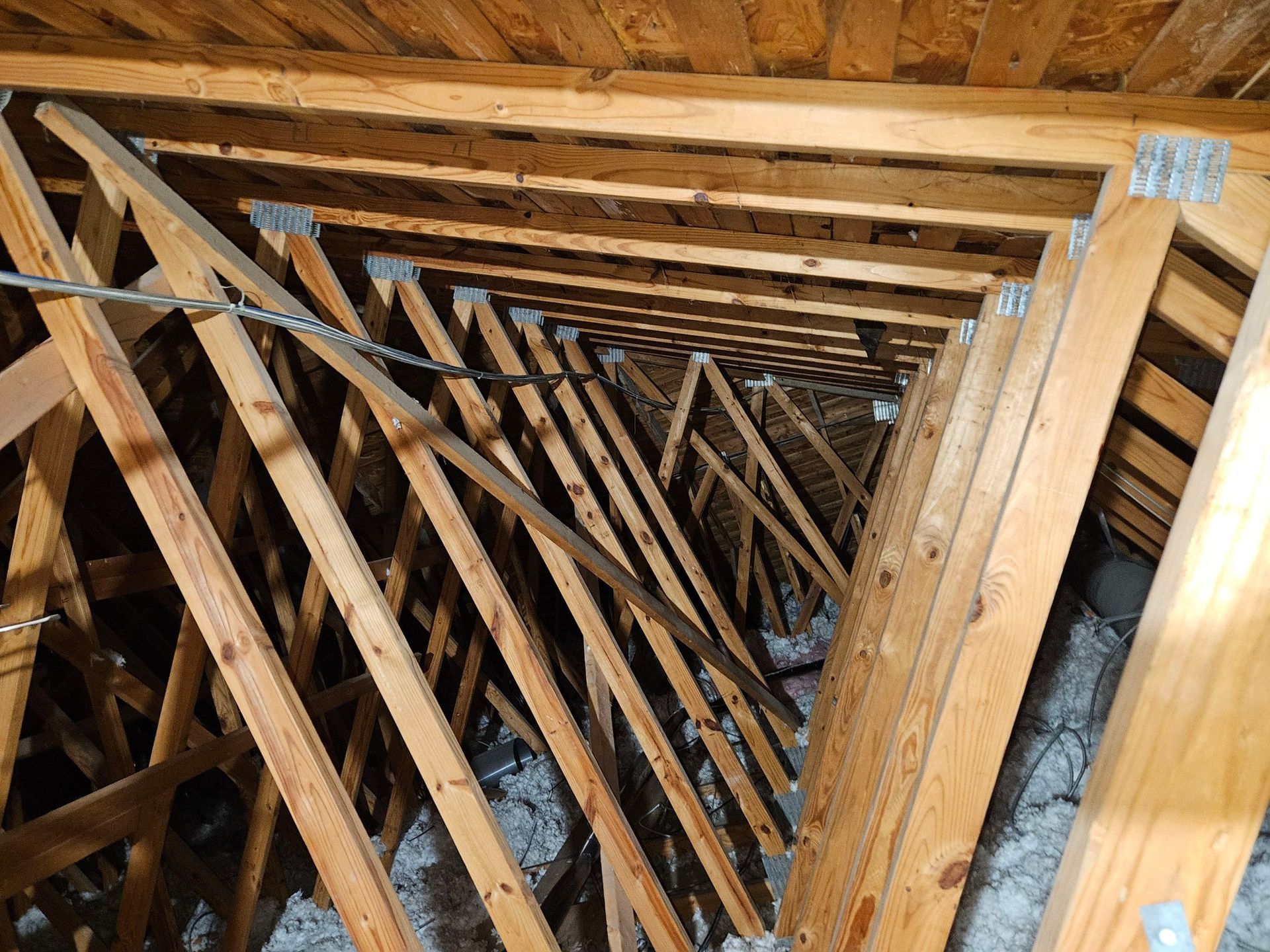 Wooden attic trusses, angled and repeated, form a triangular tunnel.