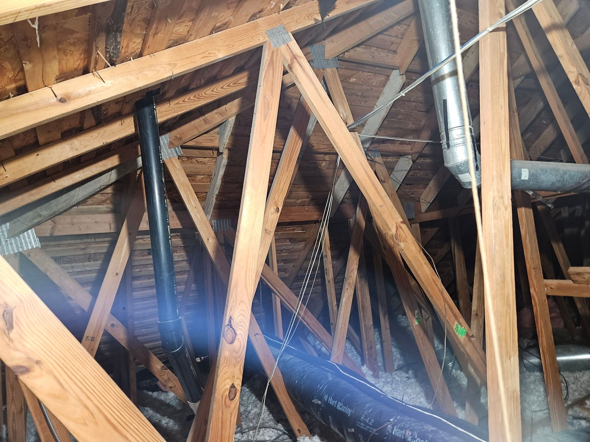 Wooden attic rafters with black and silver pipes.