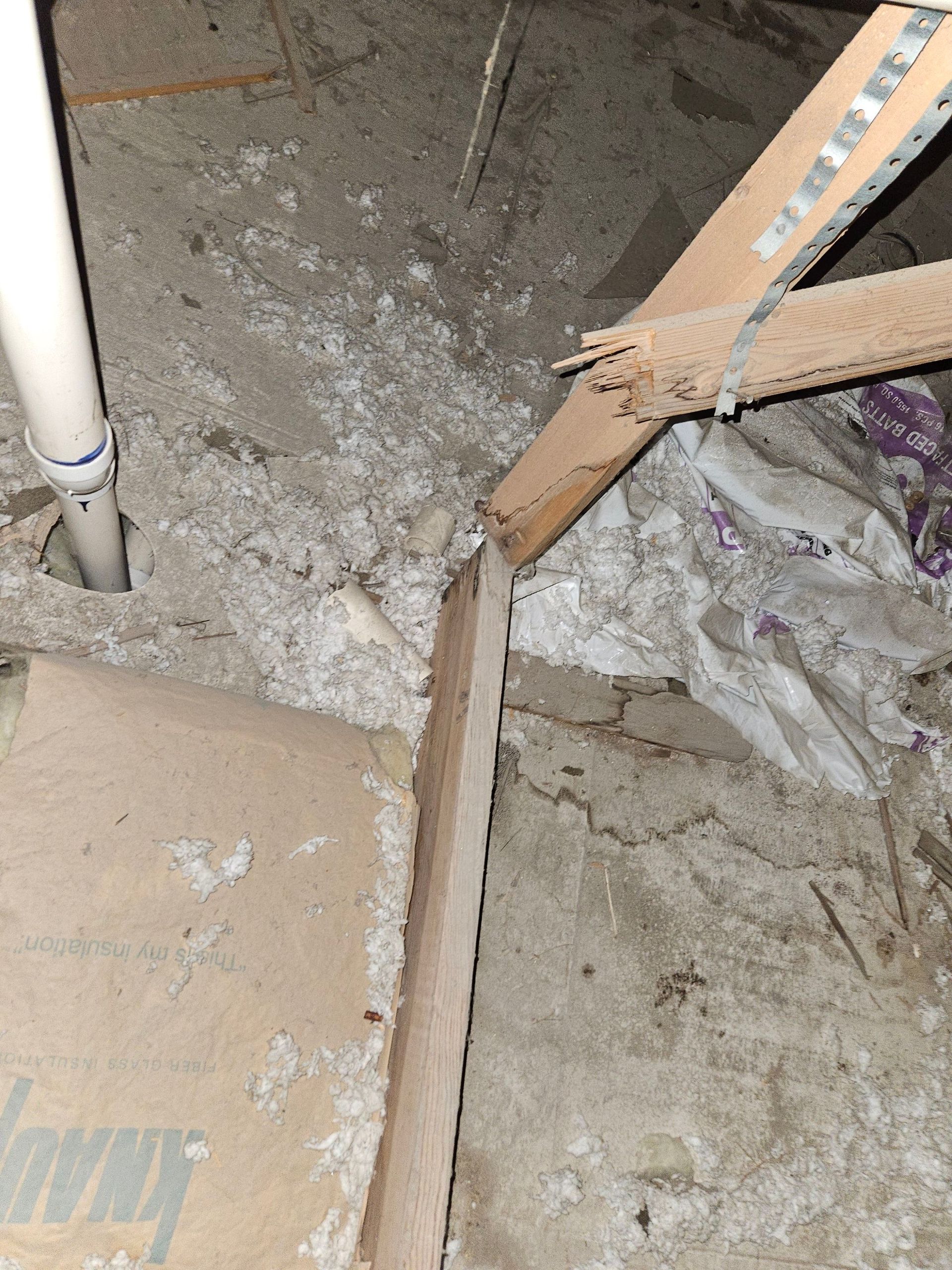 Beige and gray basement area with white pipe, wooden supports, and debris.