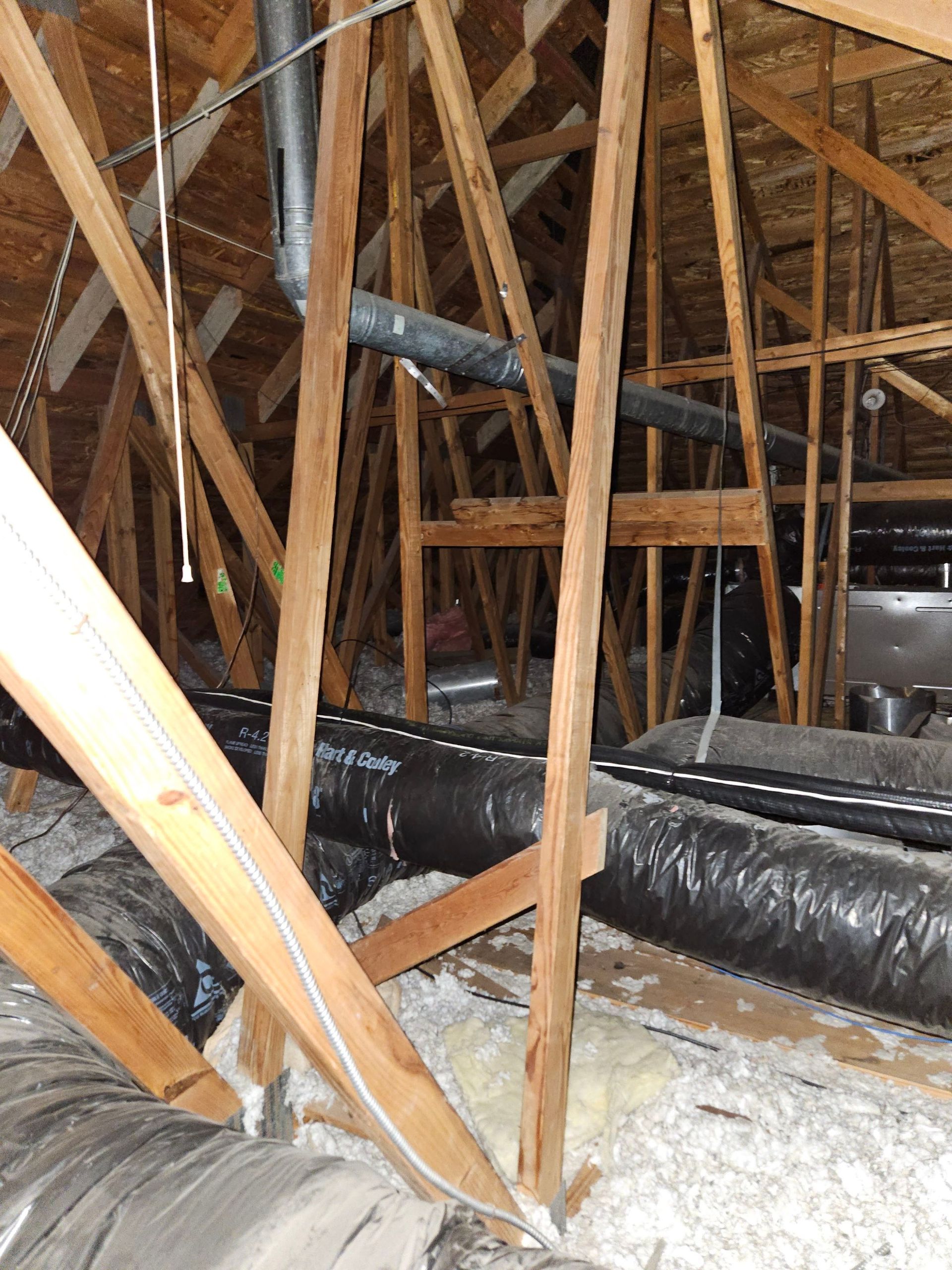 Wooden attic framing with insulation, ductwork, and a metal vent pipe.