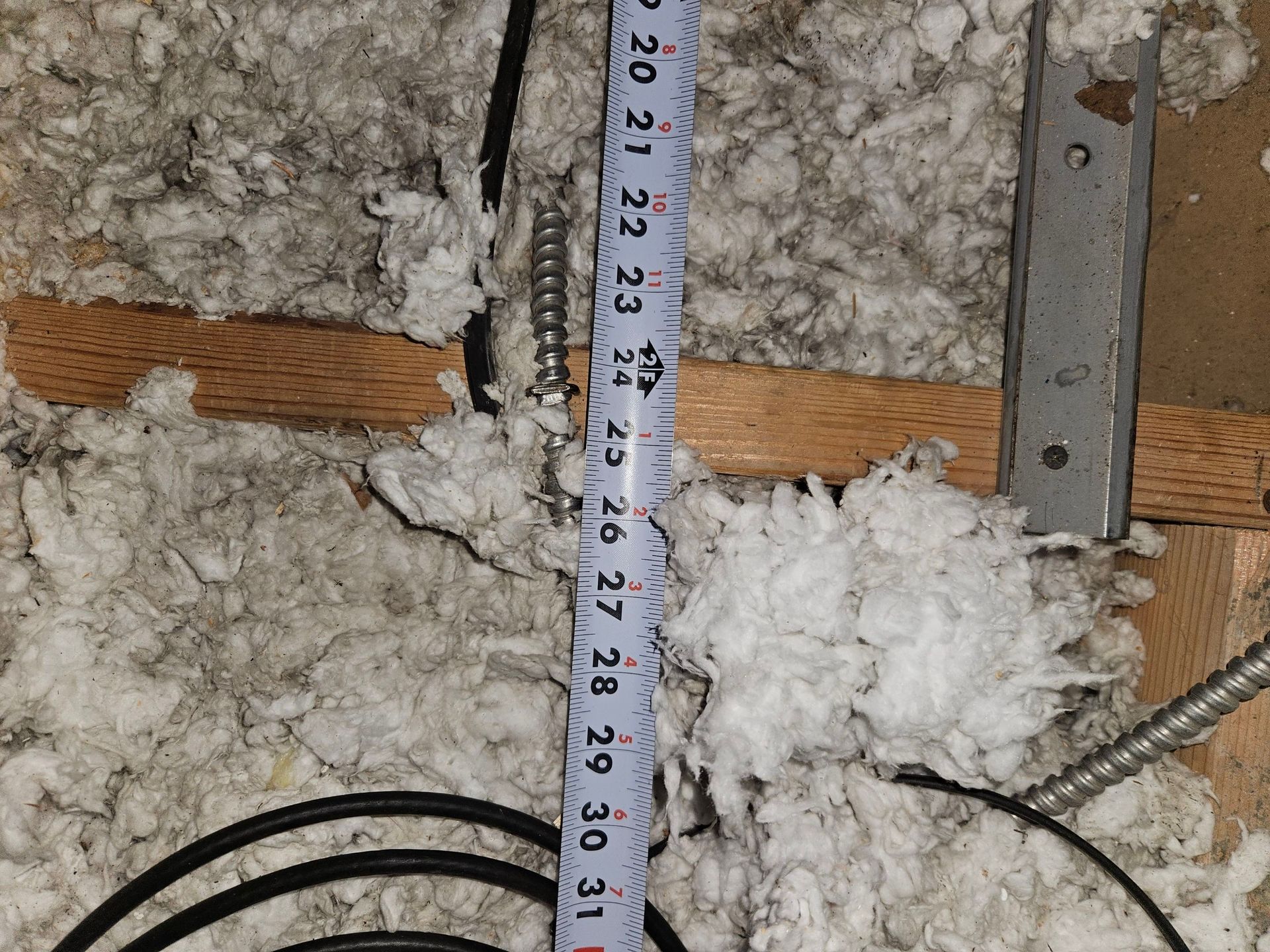 Tape measure laid on insulation in an attic, showing a measurement of 30 inches.