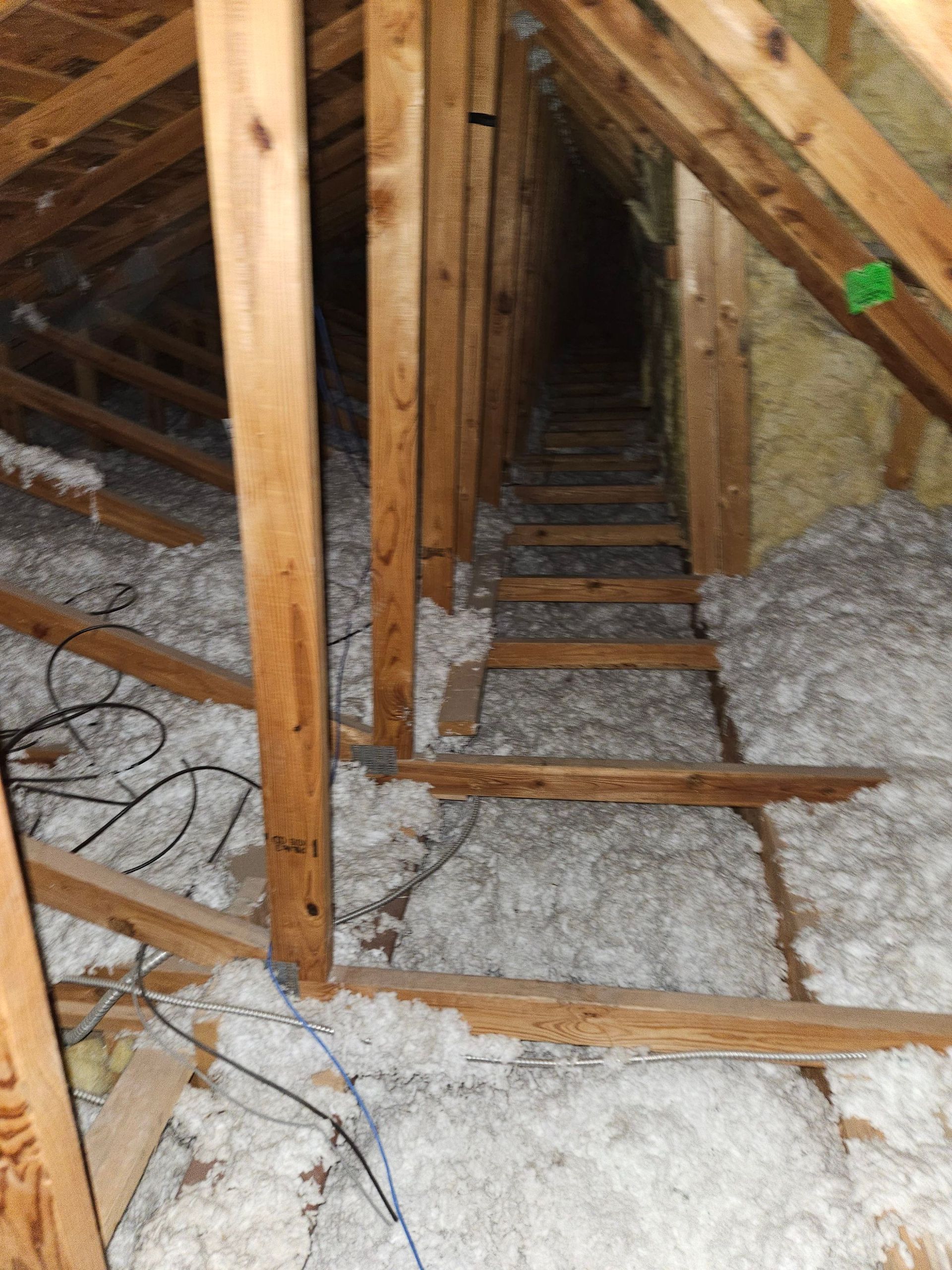 Attic interior with wooden beams, insulation, and a makeshift ladder leading into the darkness.
