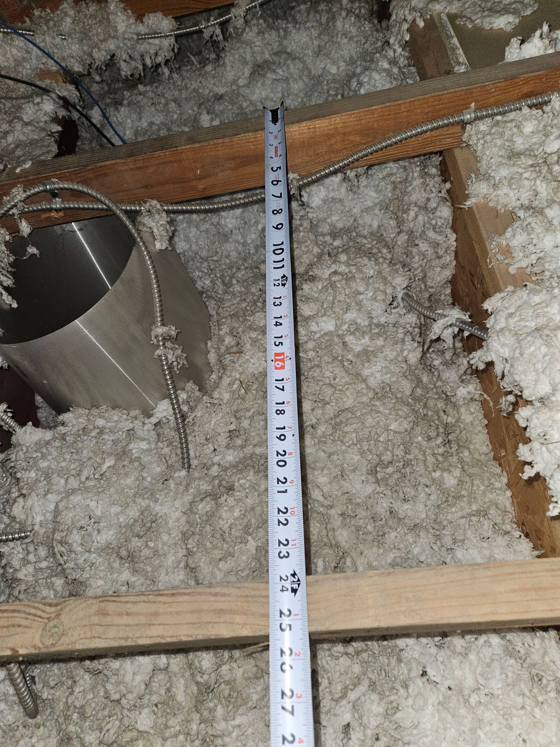 Tape measure in attic amongst insulation and ductwork.