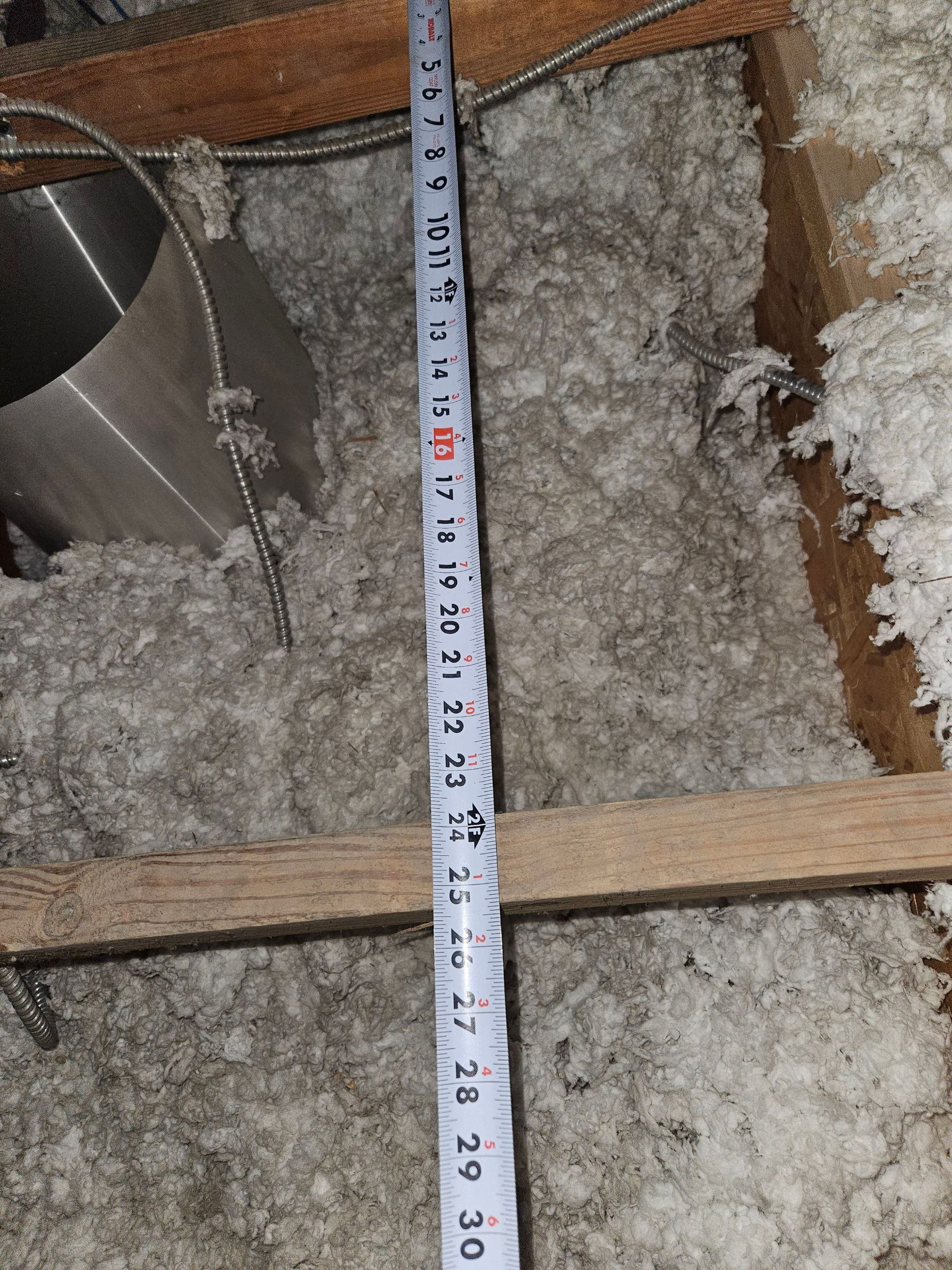 Tape measure in an attic, next to insulation and metal pipe.