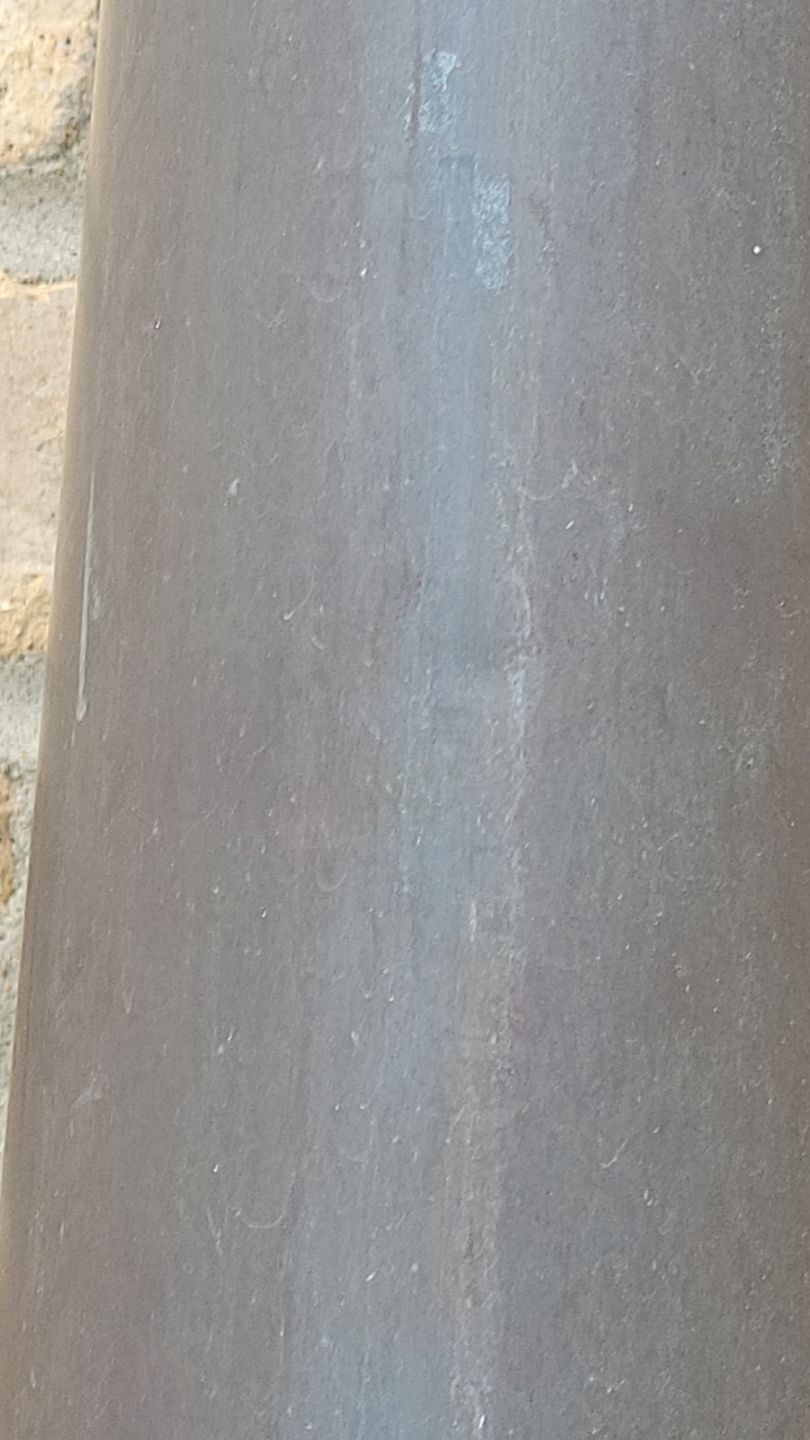 Close-up of a dark gray cylinder with subtle texture, next to a blurred brick wall.