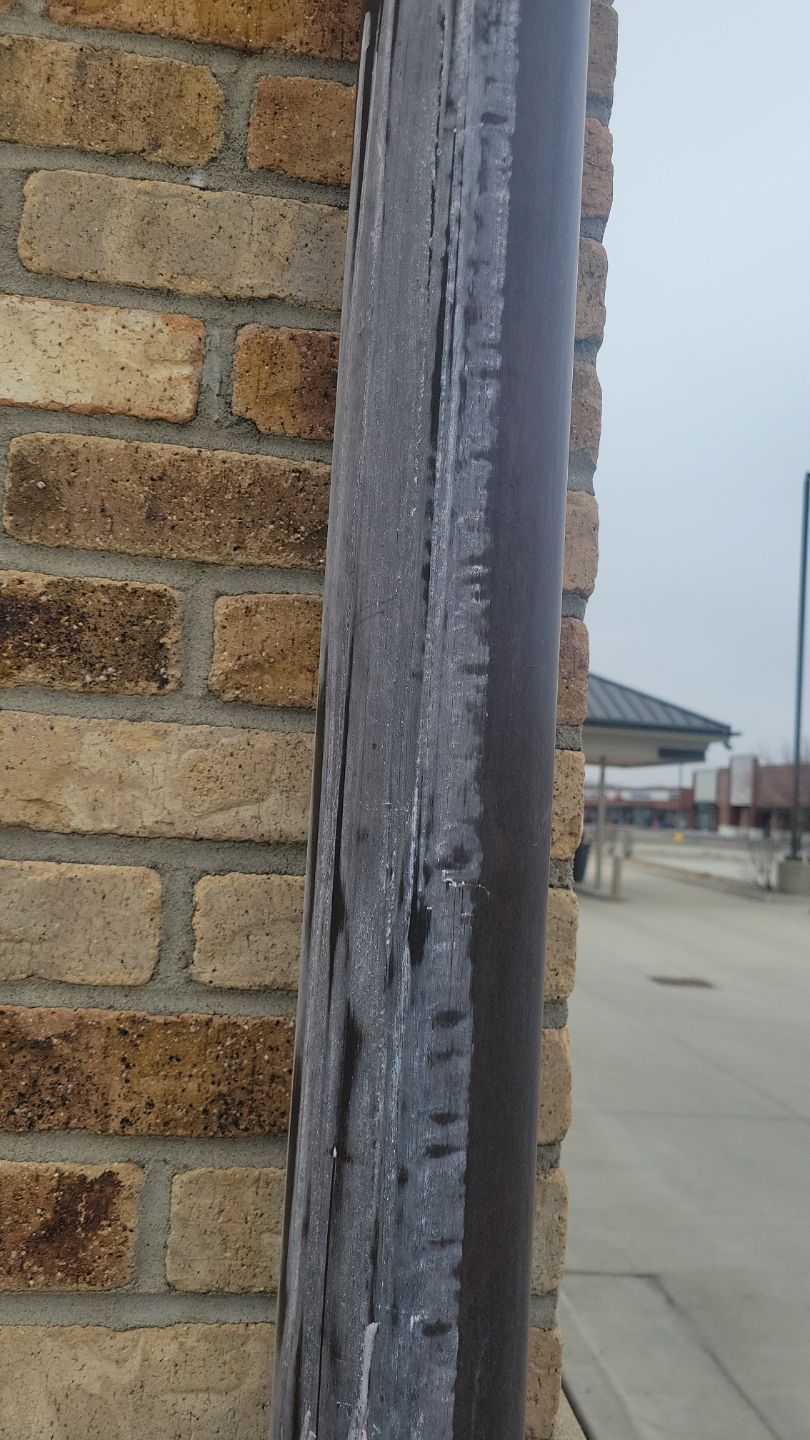 Ice clinging to a dark metal gutter on a brick building; overcast outdoor scene.