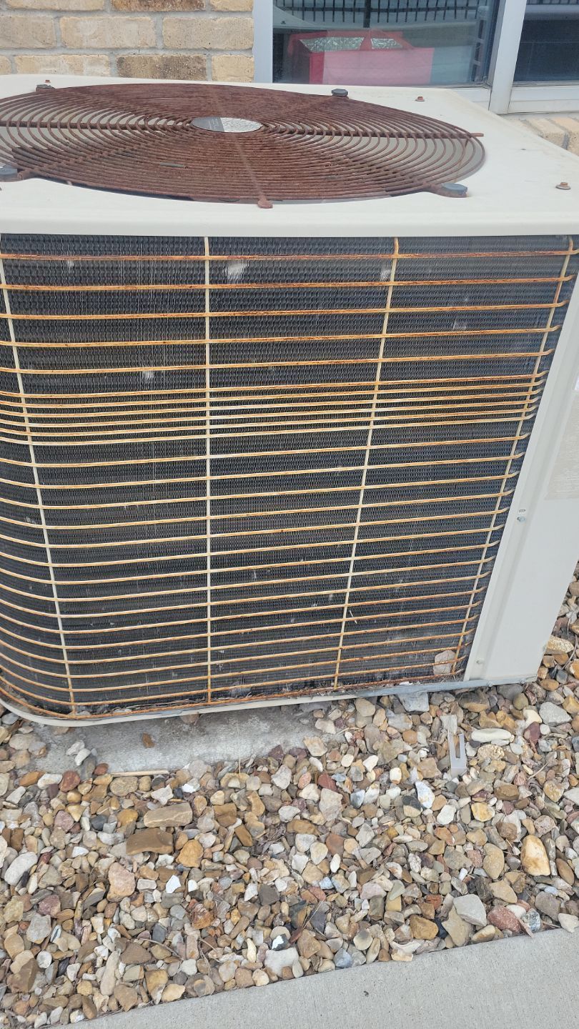 Rusty air conditioning unit with grimy coils, set on gravel.