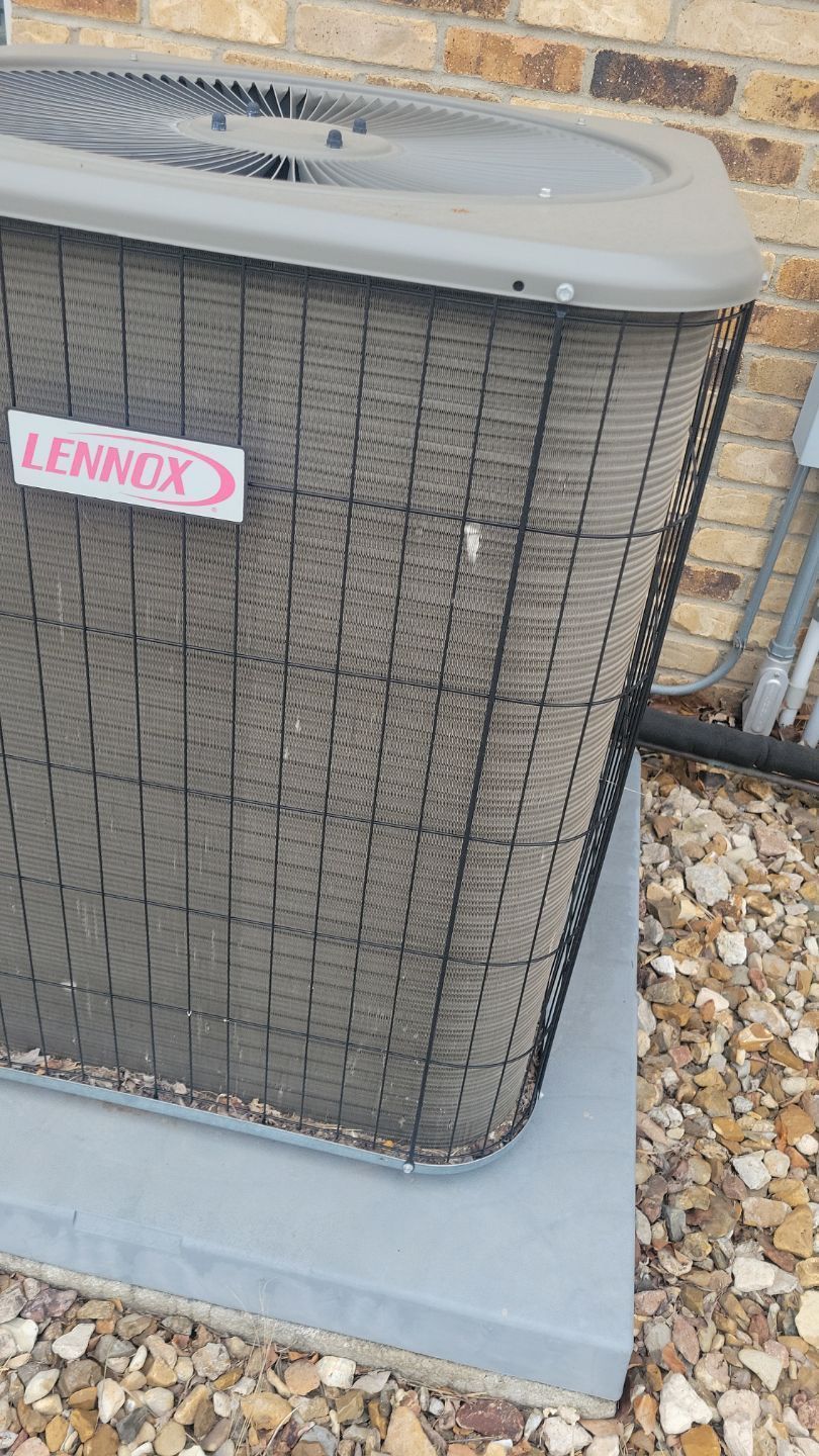 A Lennox air conditioning unit, covered in debris, sits outside on a concrete base with a brick wall backdrop.
