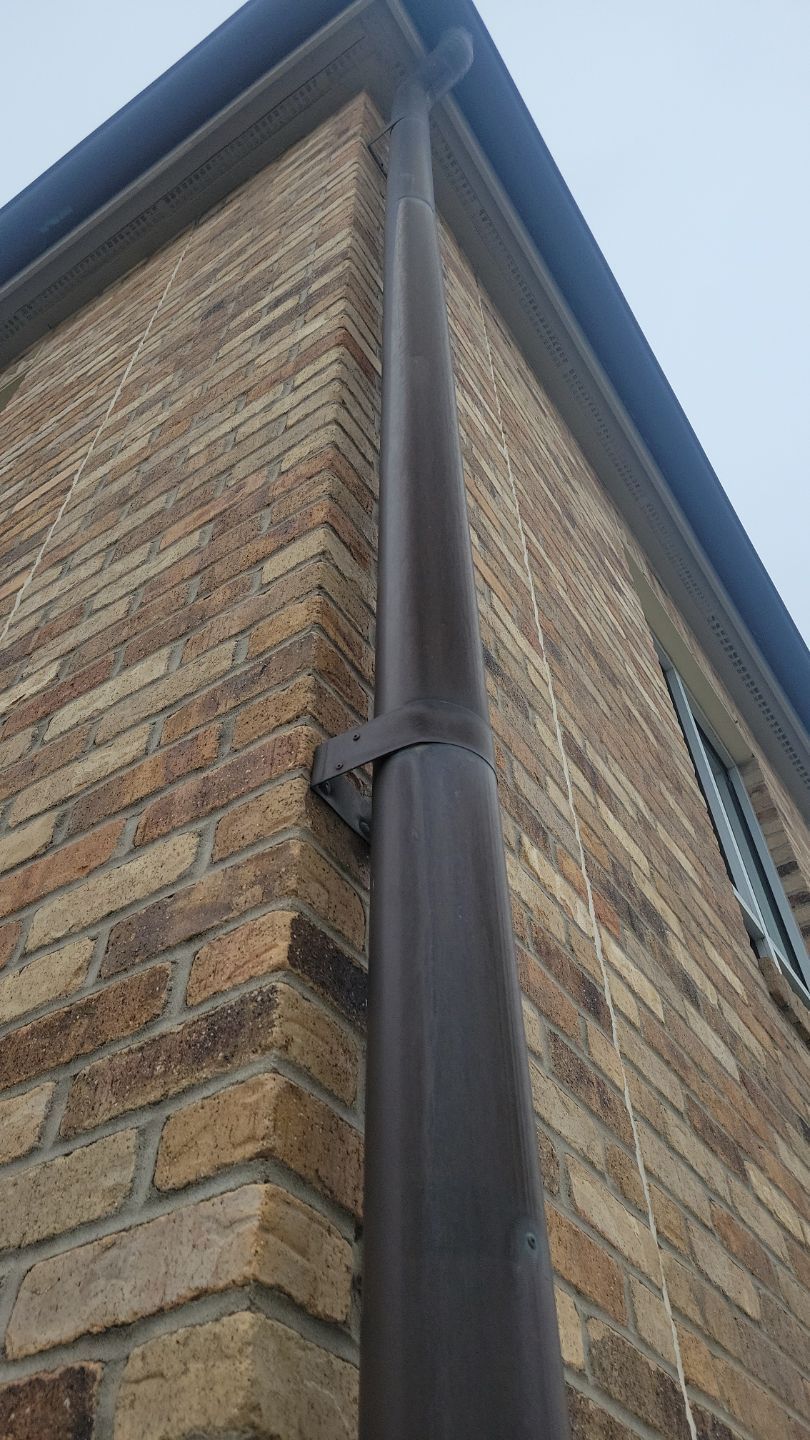Brown gutter pipe attached to a brick building's corner by a bracket.