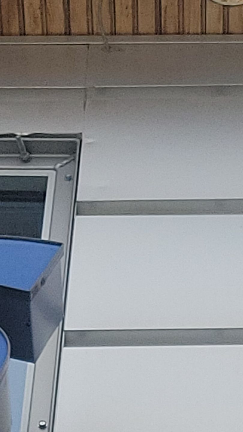 Corner of a building with a blue awning, window, and white and gray siding.