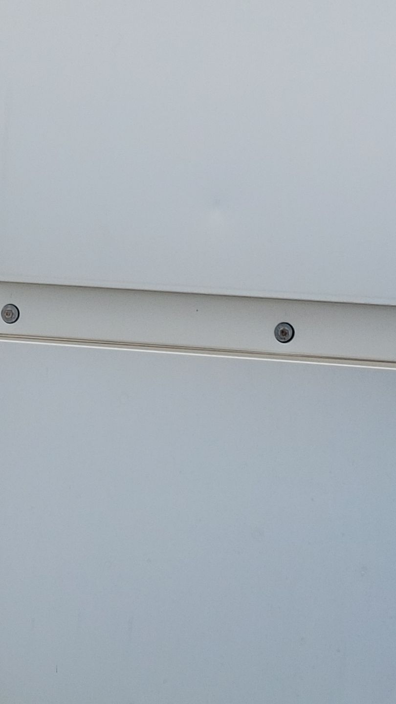 Two screws on a light-colored horizontal metal strip against a white background.