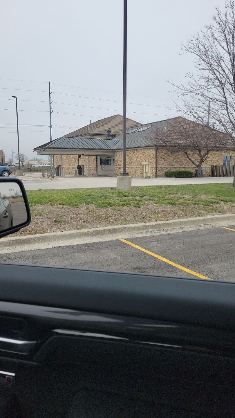 A brick building with a dark roof, likely a bank, from a car window on a cloudy day.