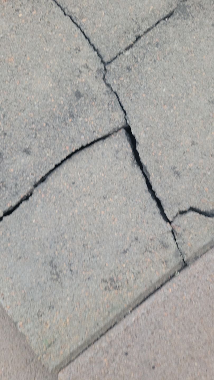 Cracked asphalt sidewalk with several long, dark cracks.