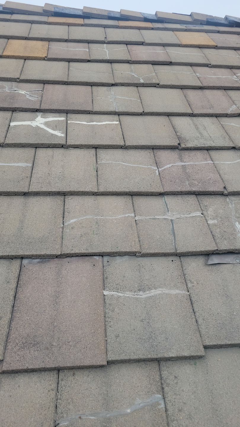 Close-up of a weathered asphalt shingle roof. Faint white lines mark cracks across several shingles.