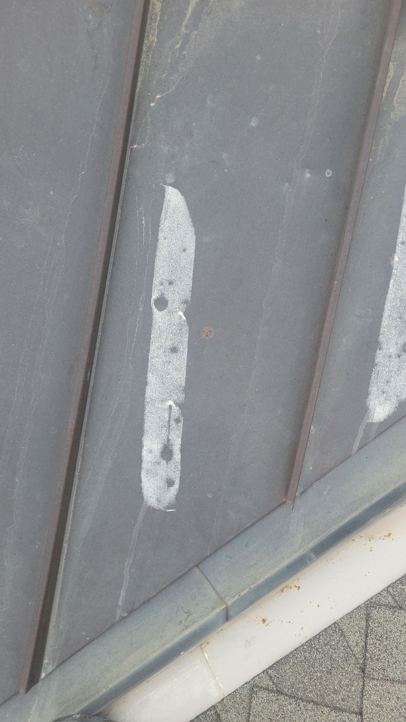 Close-up of gray metal roof with a white, vertical, irregular-shaped mark and some small dark spots.