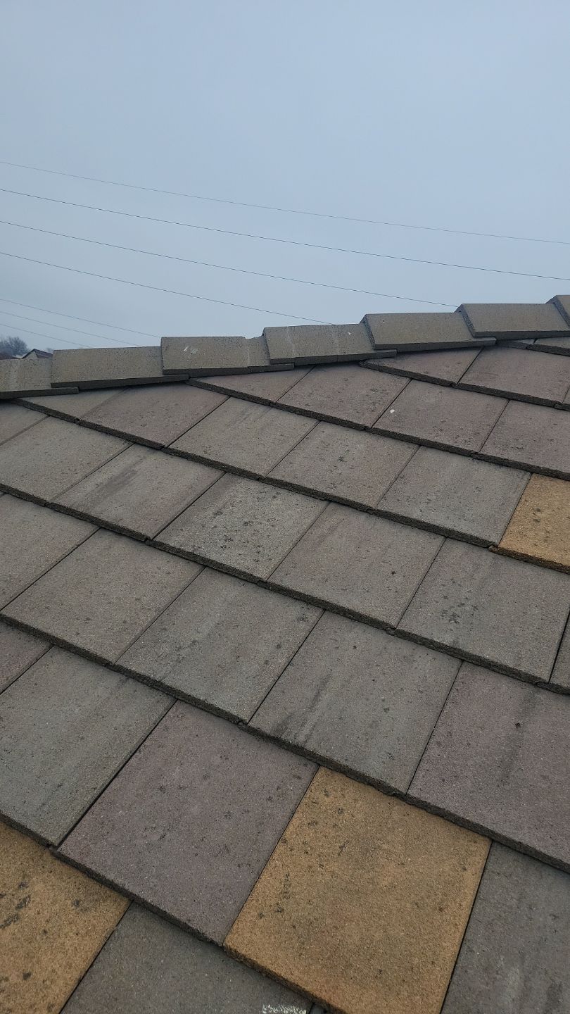 Close-up of a roof with brown and tan tiles against a cloudy sky.